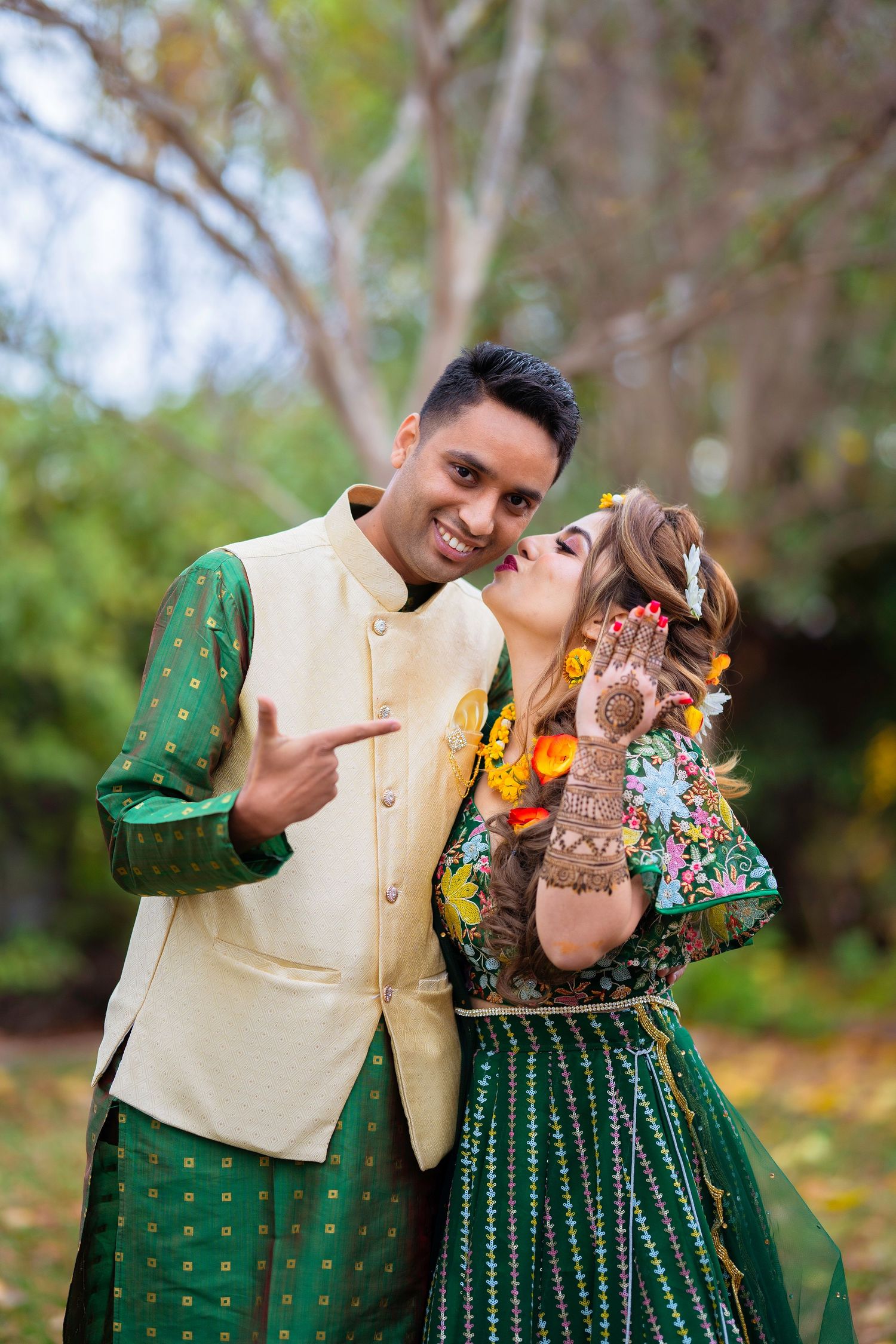 Playful moment between couple in matching green and cream Indian wedding outfits.