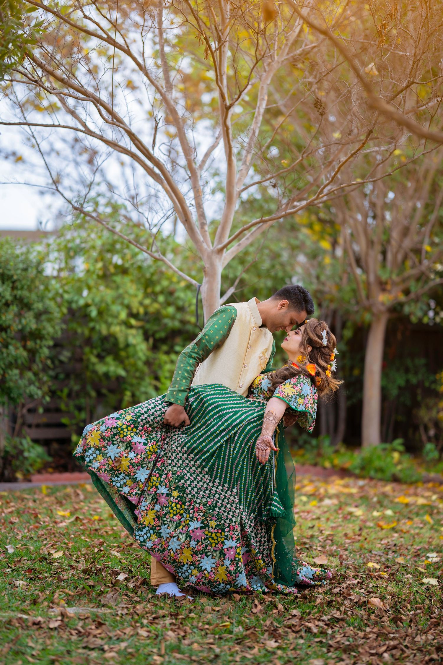 Romantic dip pose between couple wearing traditional Indian wedding attire in garden setting.