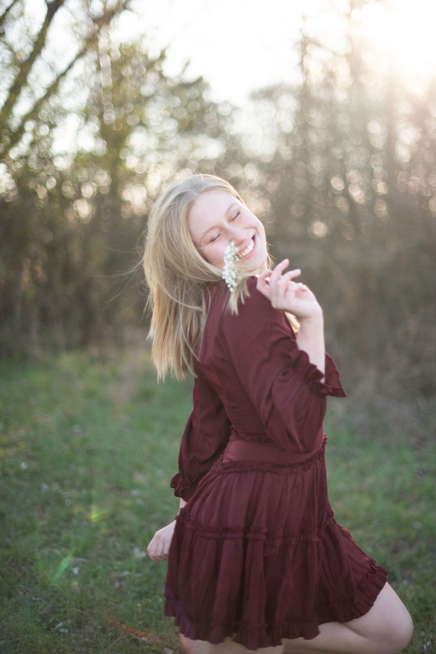 Joyful twirl in burgundy dress captured during golden hour outdoor photoshoot.