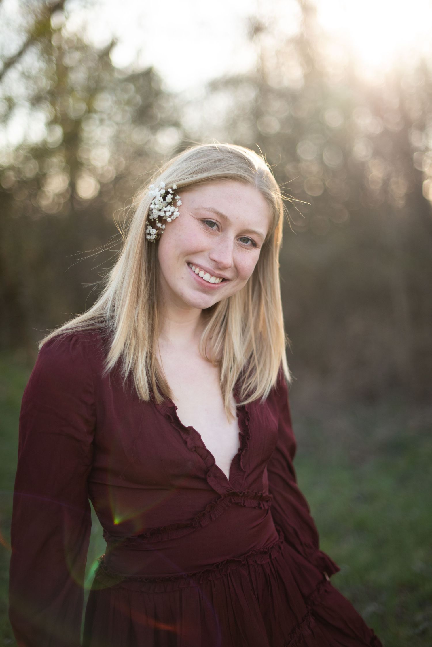 Portrait of someone in a burgundy dress with flowers in their hair against a natural outdoor background.