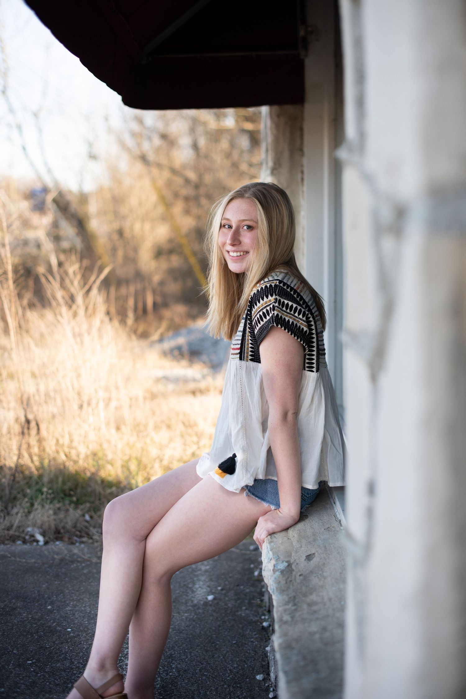 Casual portrait of someone sitting on a concrete ledge wearing shorts and a patterned top.