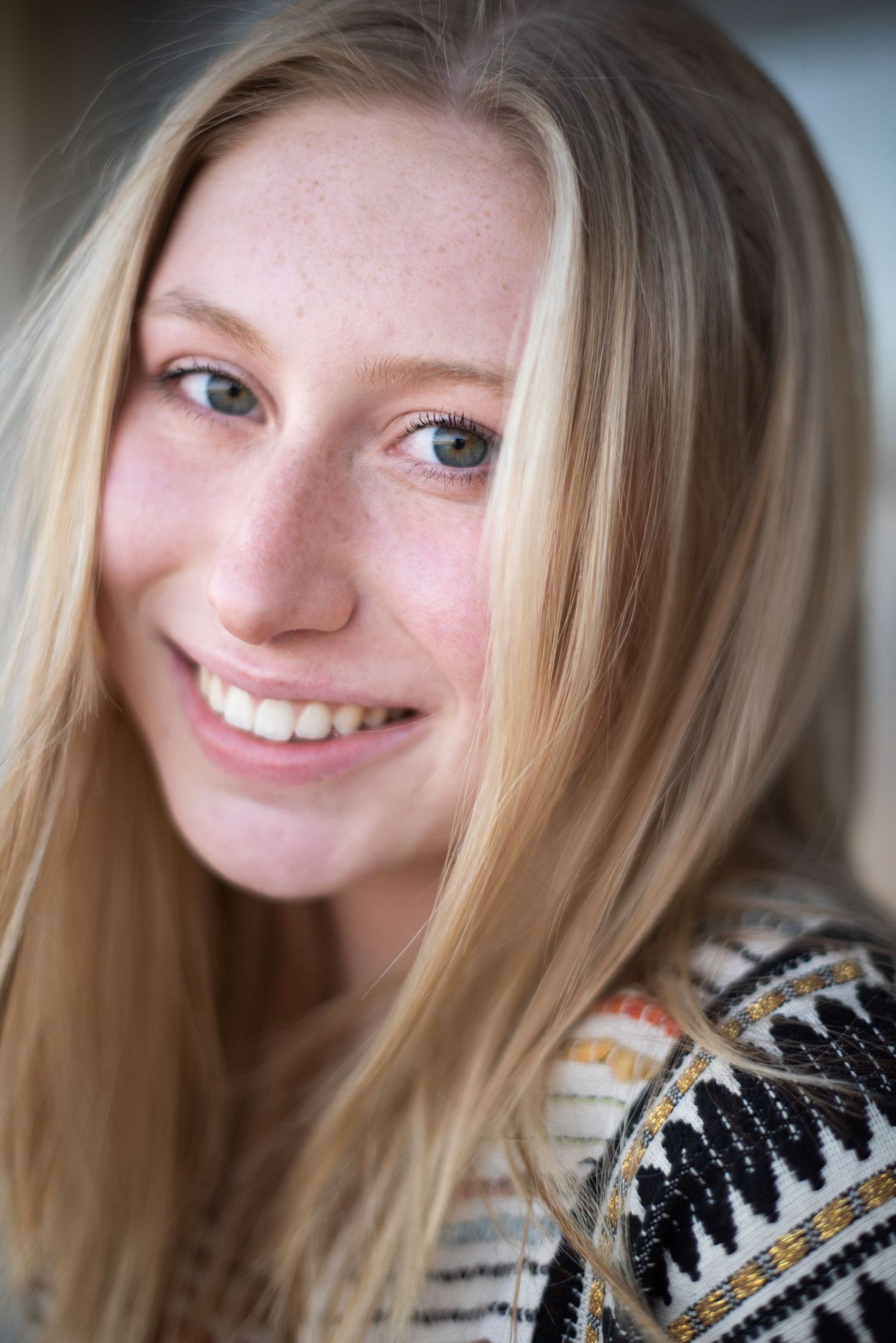 Close up portrait of a smiling person with long blonde hair wearing a patterned sweater.