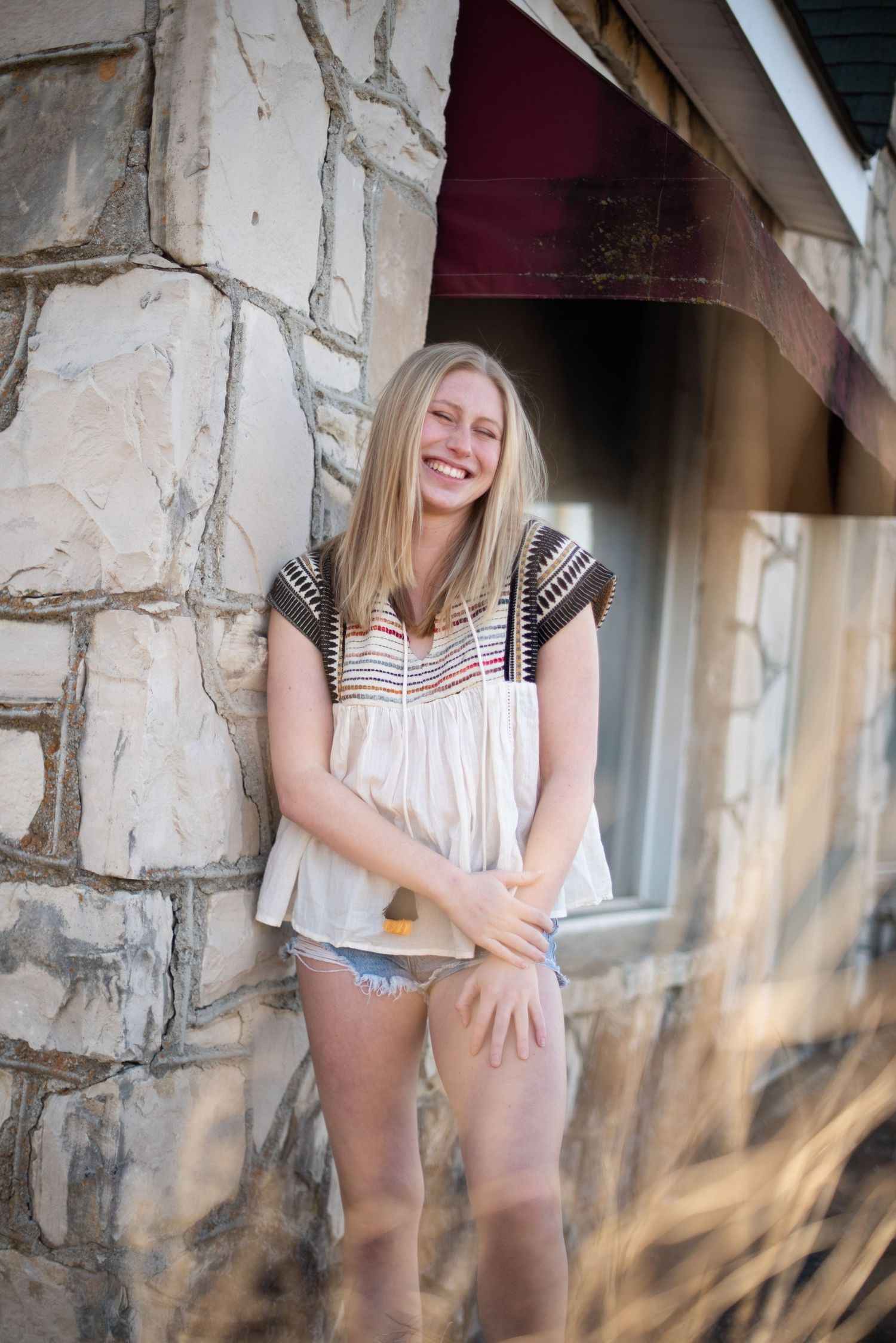 Candid outdoor shot by stone wall showing joyful expression in casual summer attire.