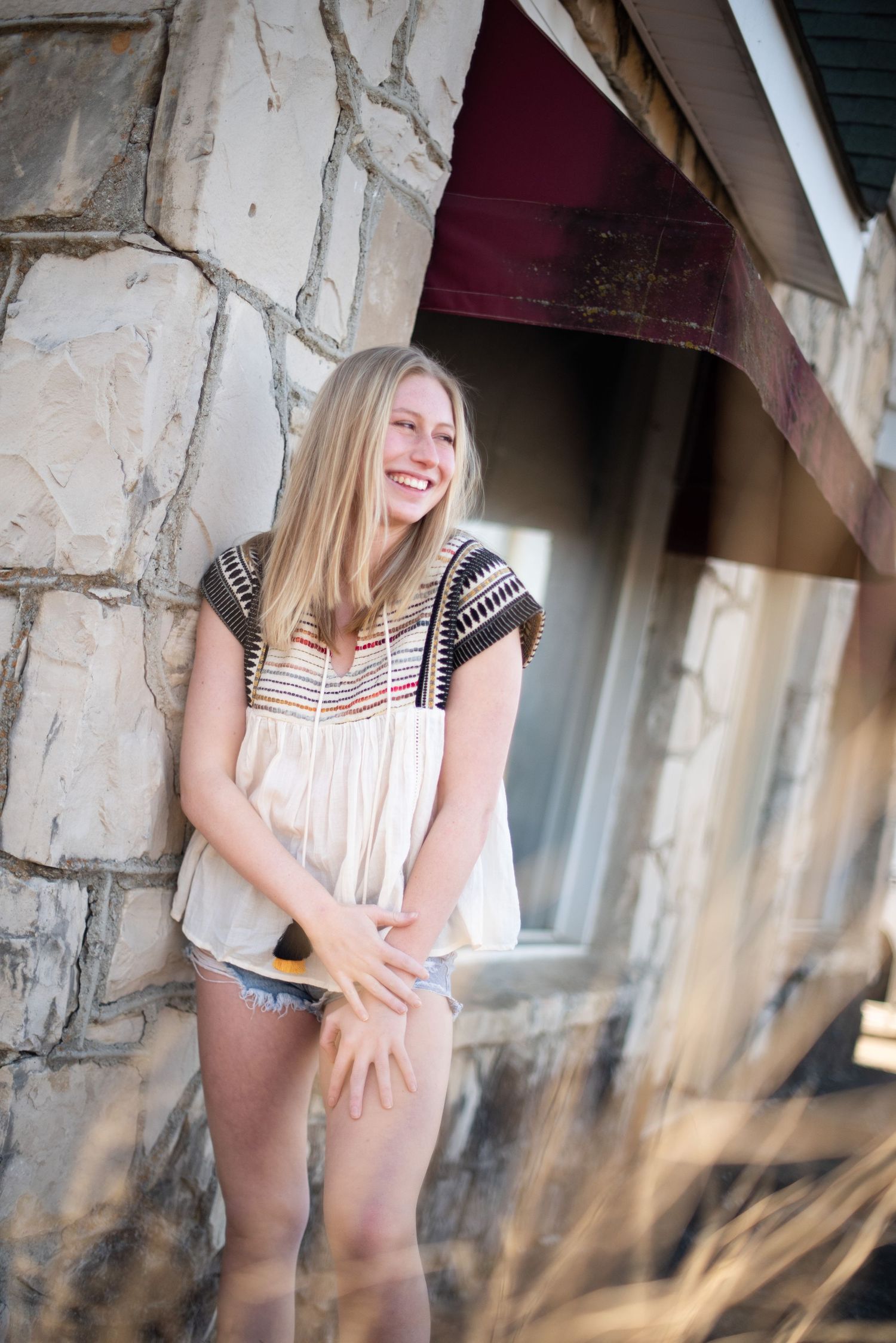 Laughing outdoor portrait against rustic stone wall backdrop in casual summer clothing.