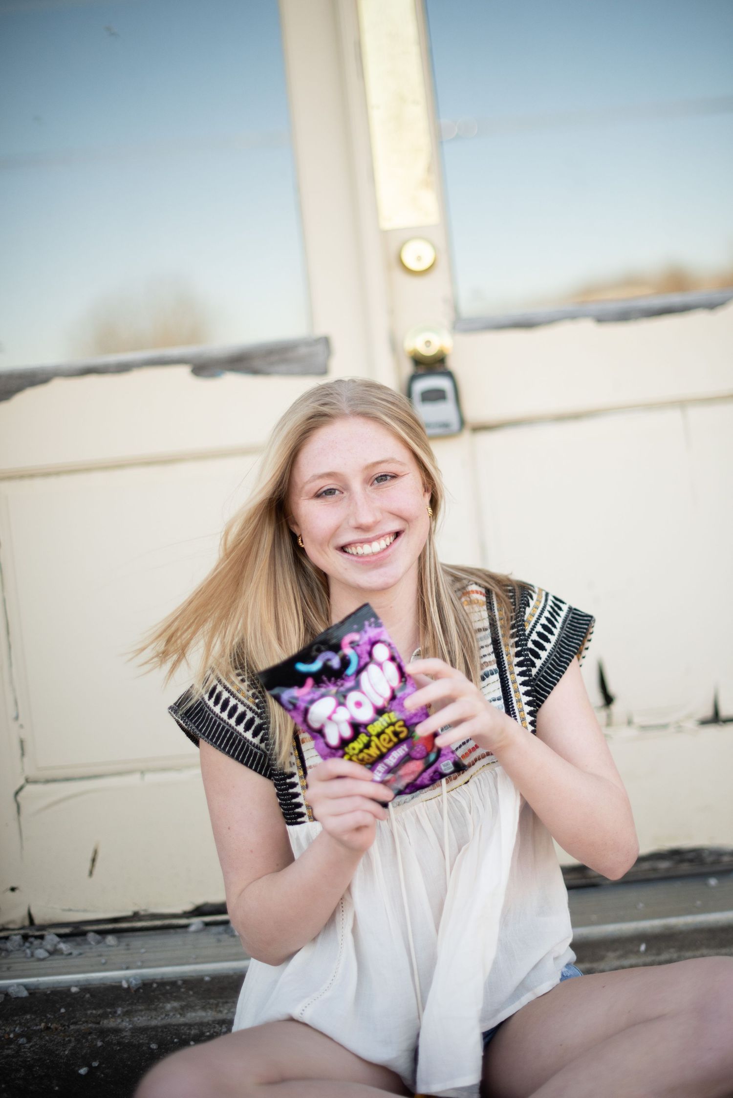 Cheerful outdoor portrait holding colorful candy against white wall background.