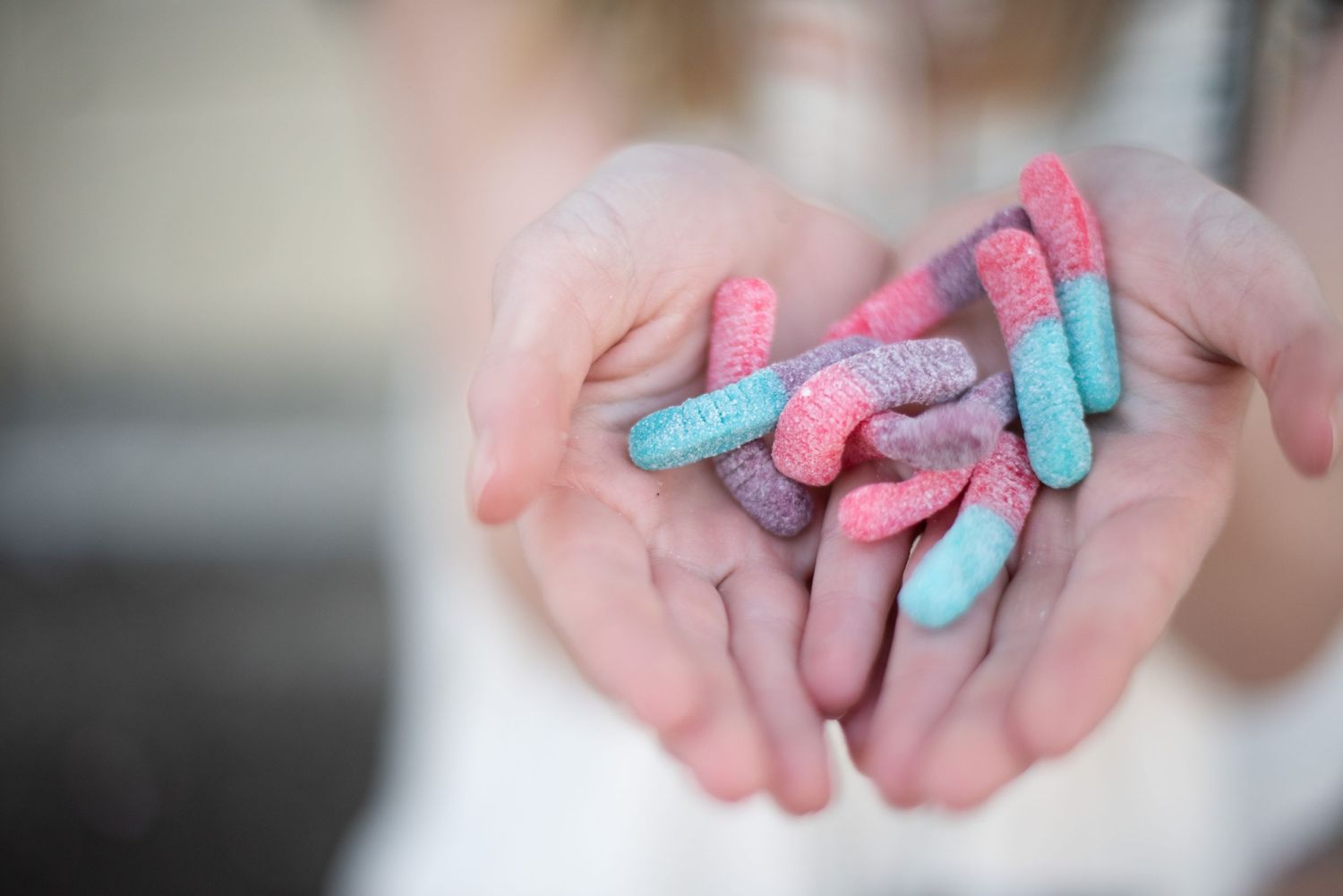 Colorful gummy candies in blue and pink held in outstretched palms.