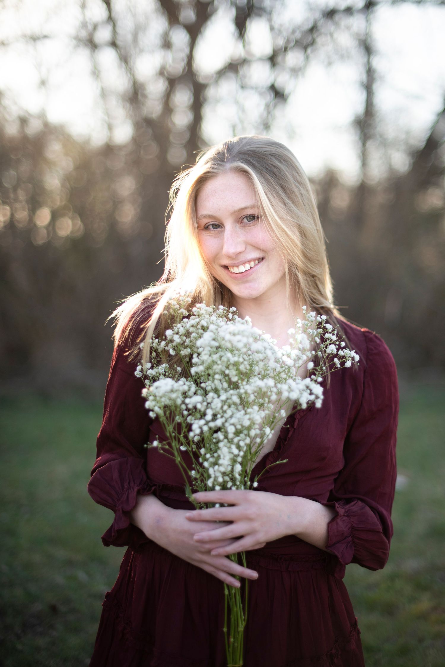 Someone holding a bouquet of baby's breath flowers while wearing a burgundy dress in a natural setting.