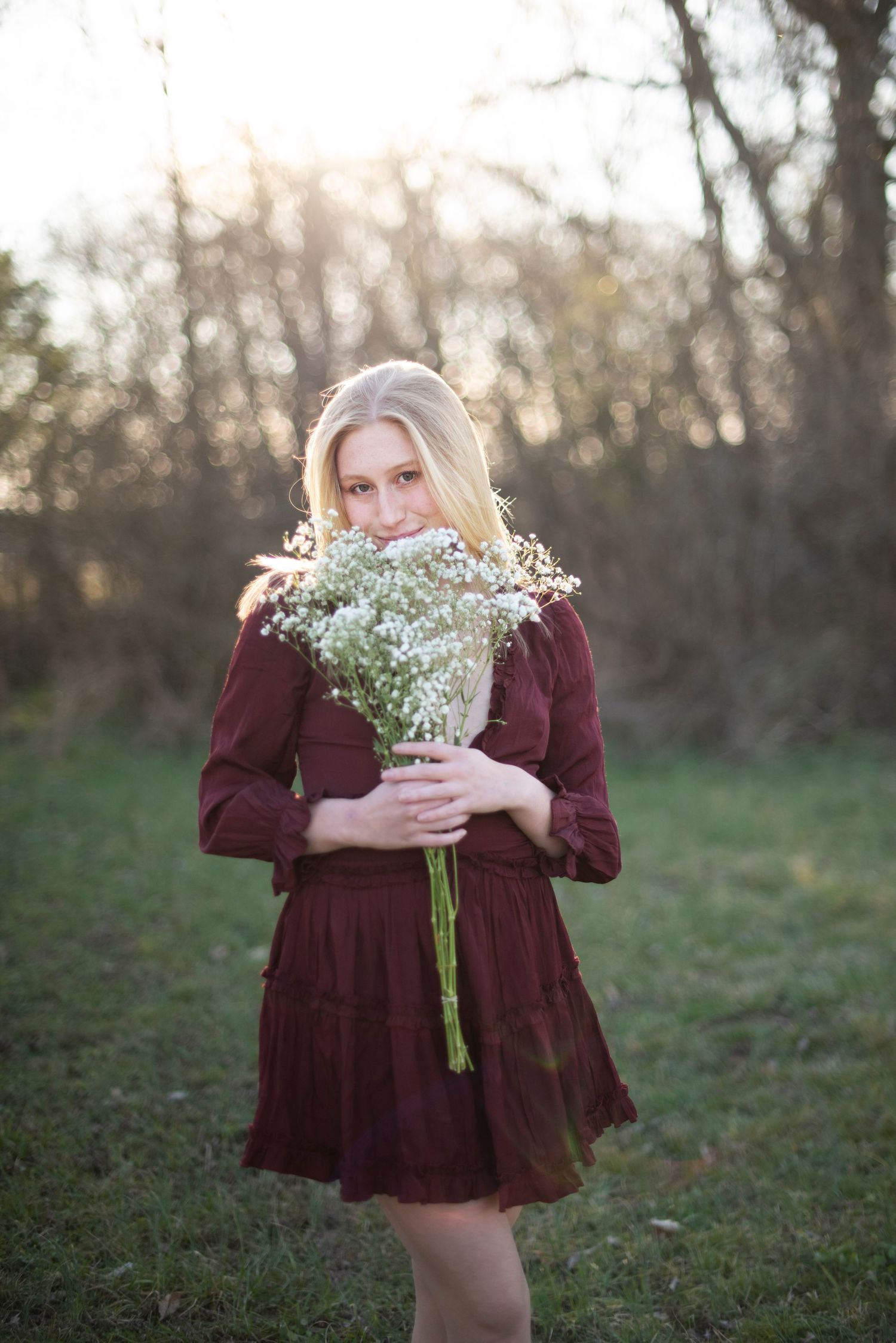 Figure in burgundy dress poses with baby's breath bouquet in an outdoor setting.