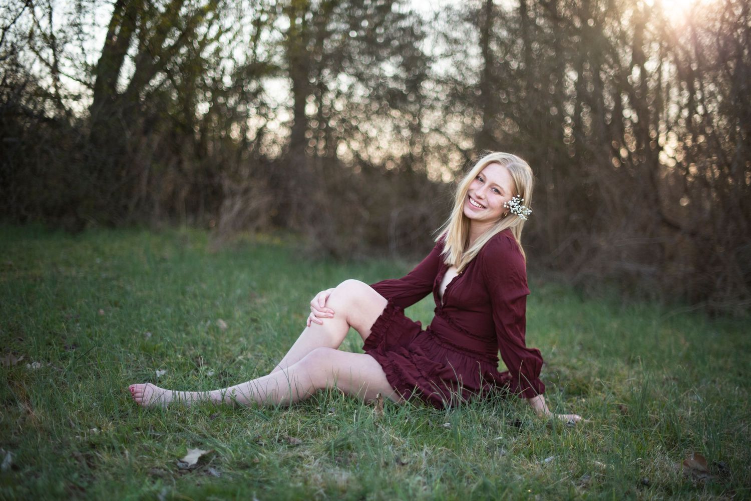 Someone in a burgundy dress sitting on grass during golden hour.