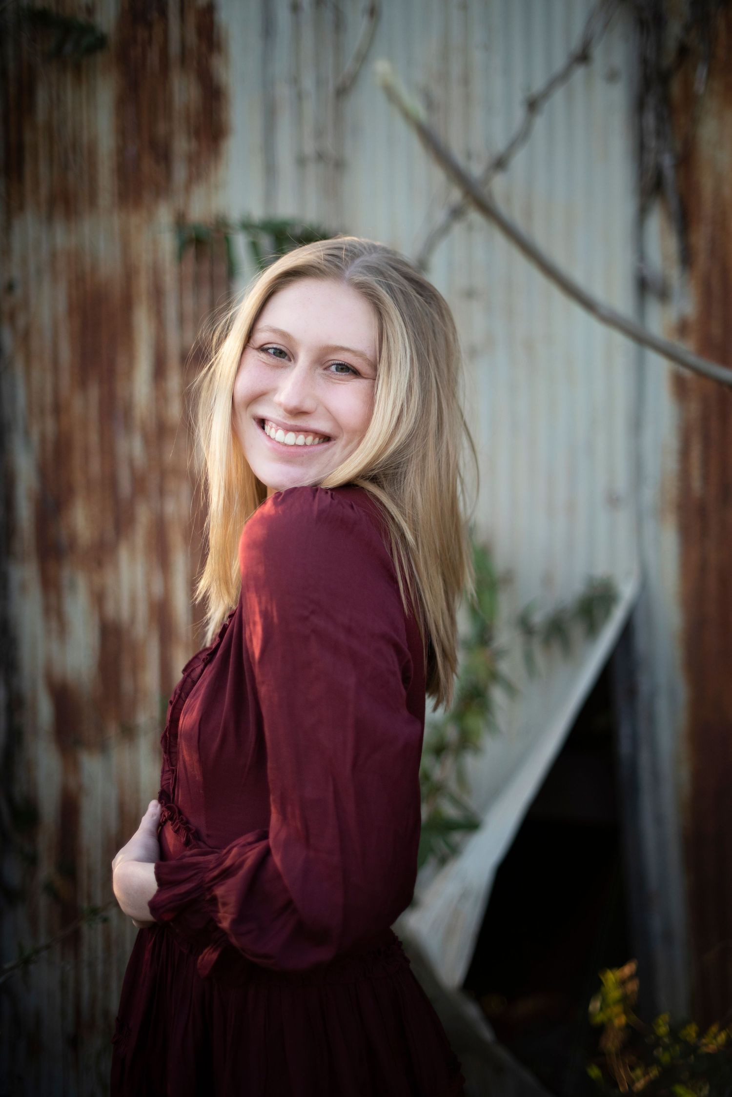 Portrait against rustic metal wall wearing burgundy dress.