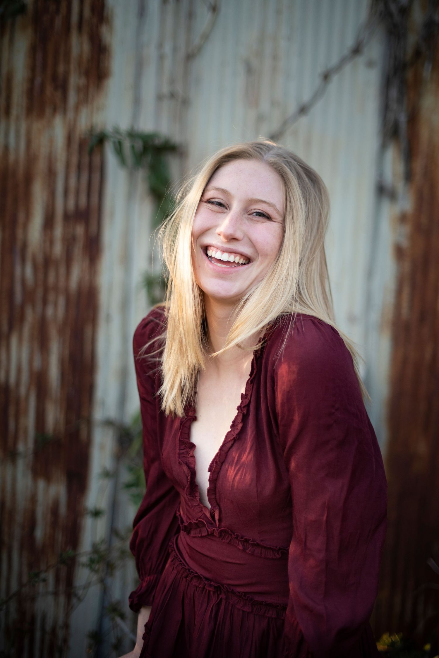Portrait against weathered metal wall in burgundy dress with natural lighting.