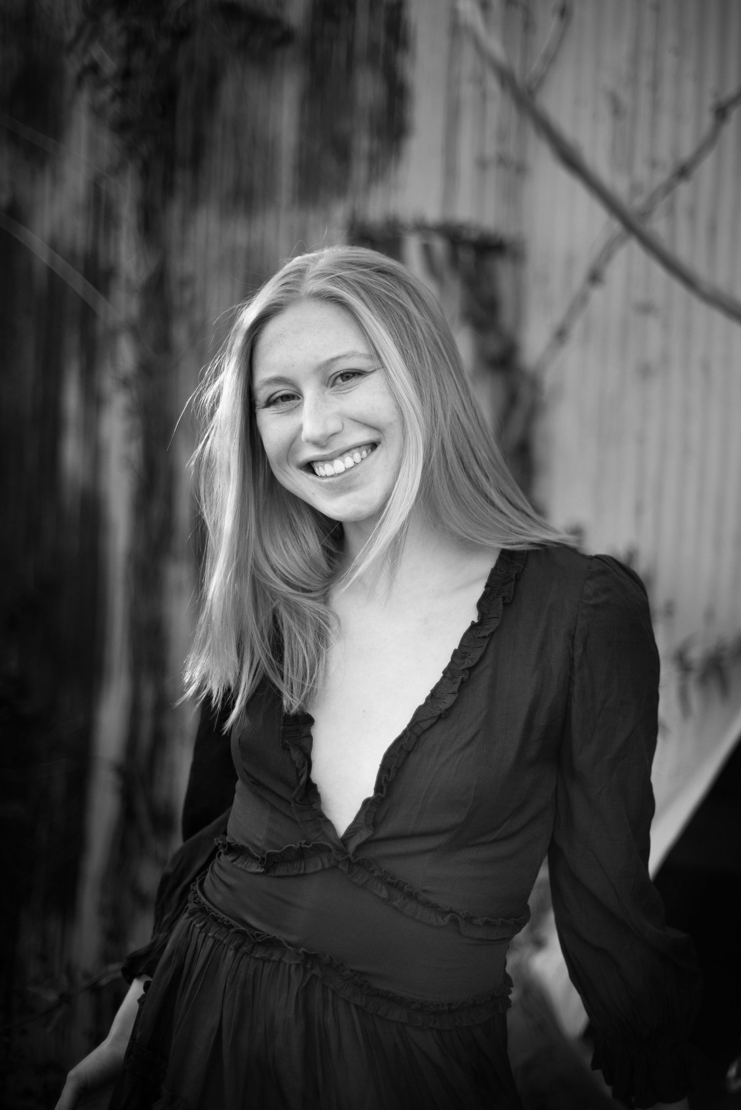 Black and white portrait of woman in dark dress smiling against rustic wooden background.