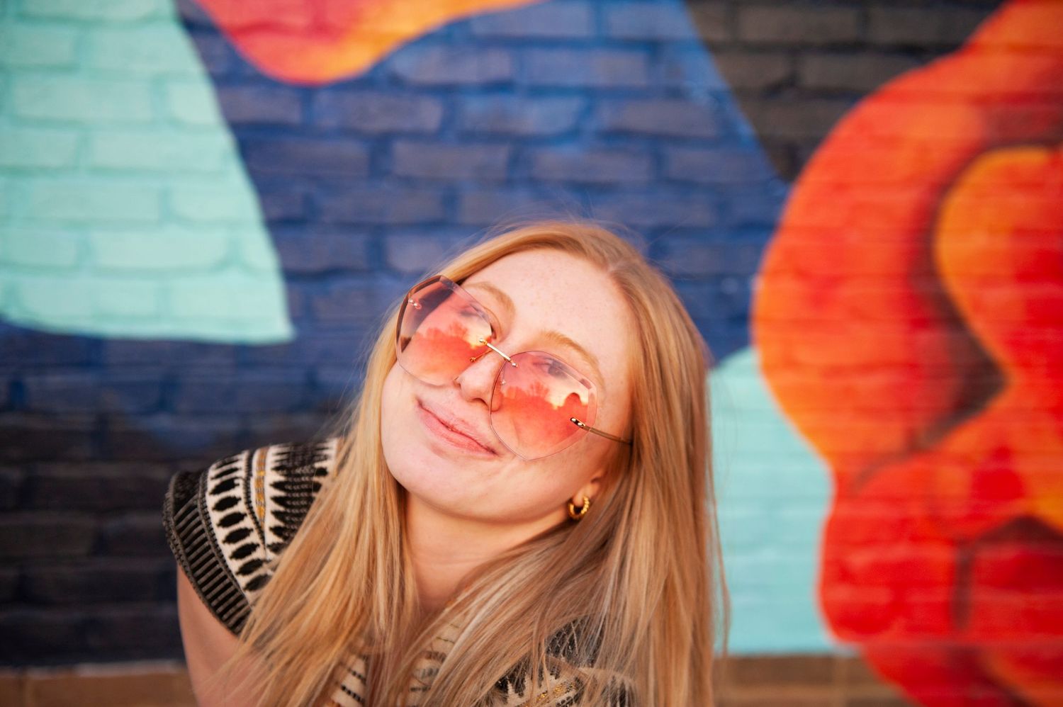 Close up portrait with rose-tinted glasses against vibrant mural background.