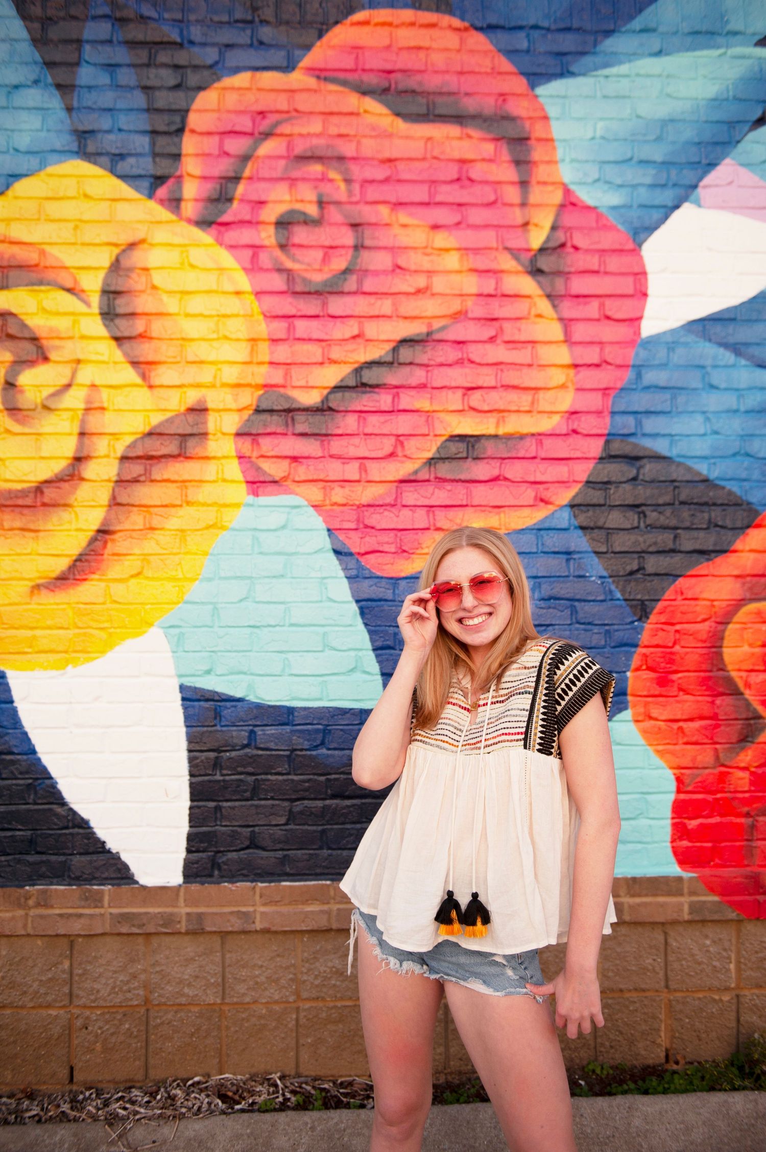 Casual summer outfit pose against large floral street art mural.