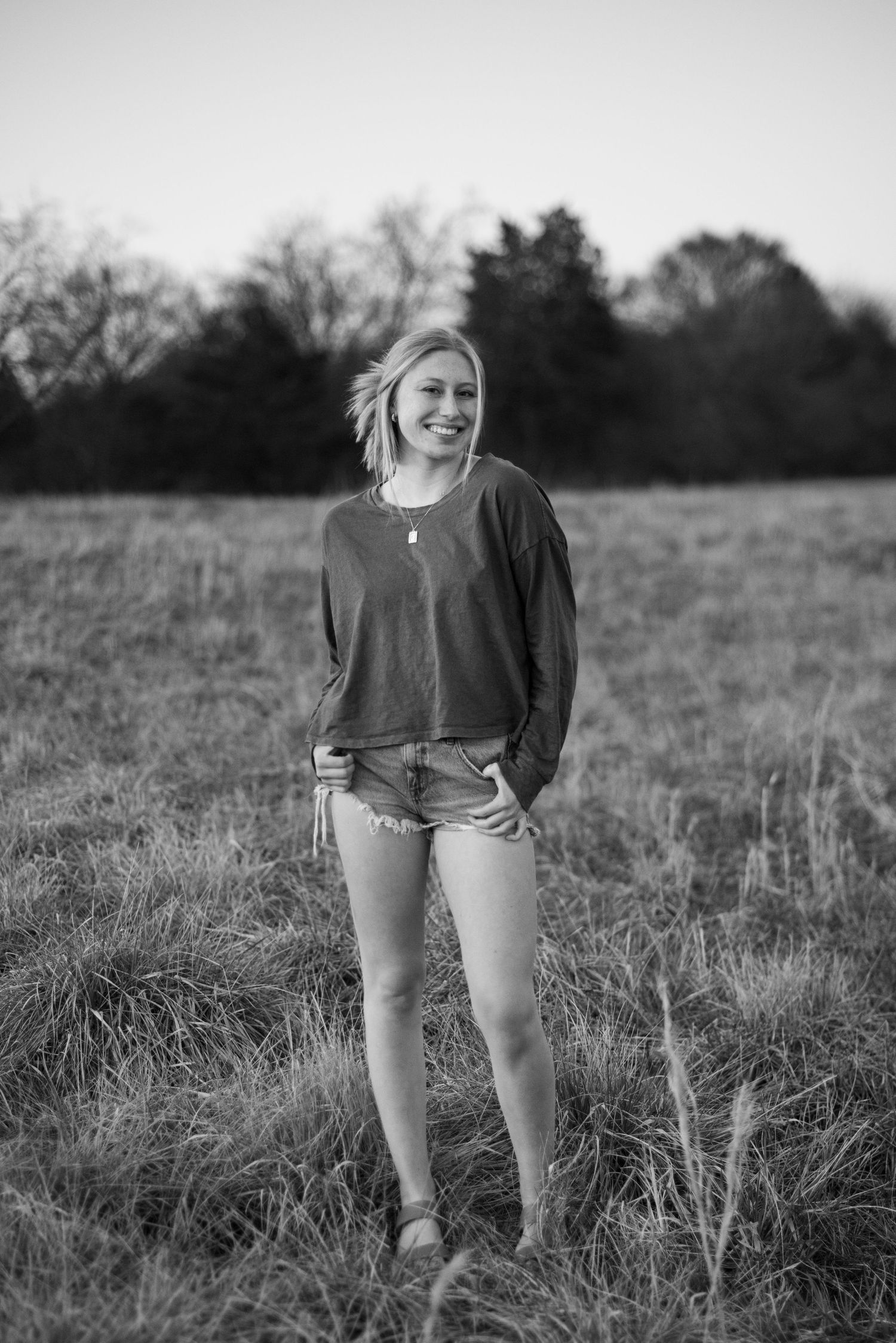 Black and white portrait in casual sweater standing in open field.