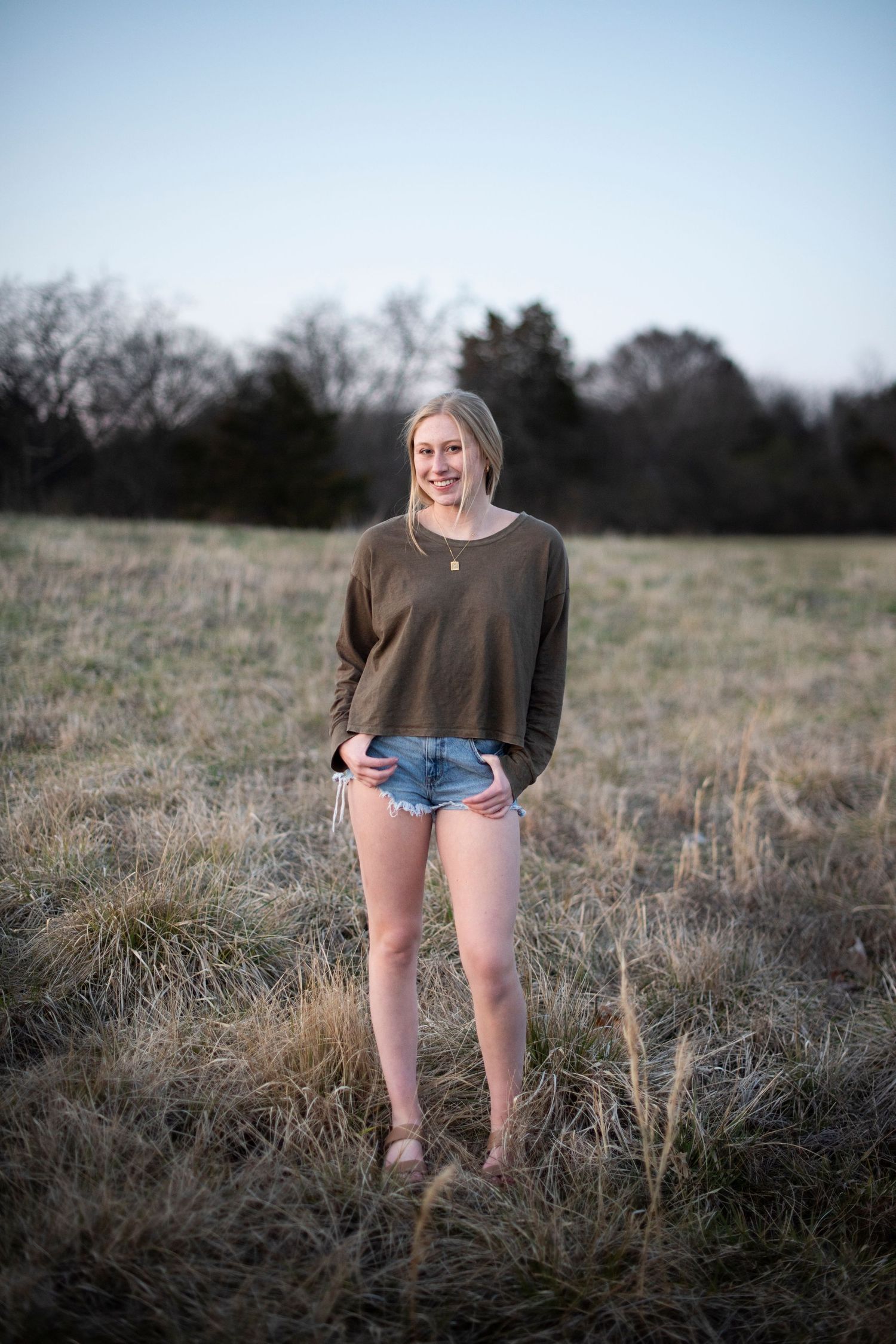 Natural outdoor portrait in brown sweater and shorts at golden hour.