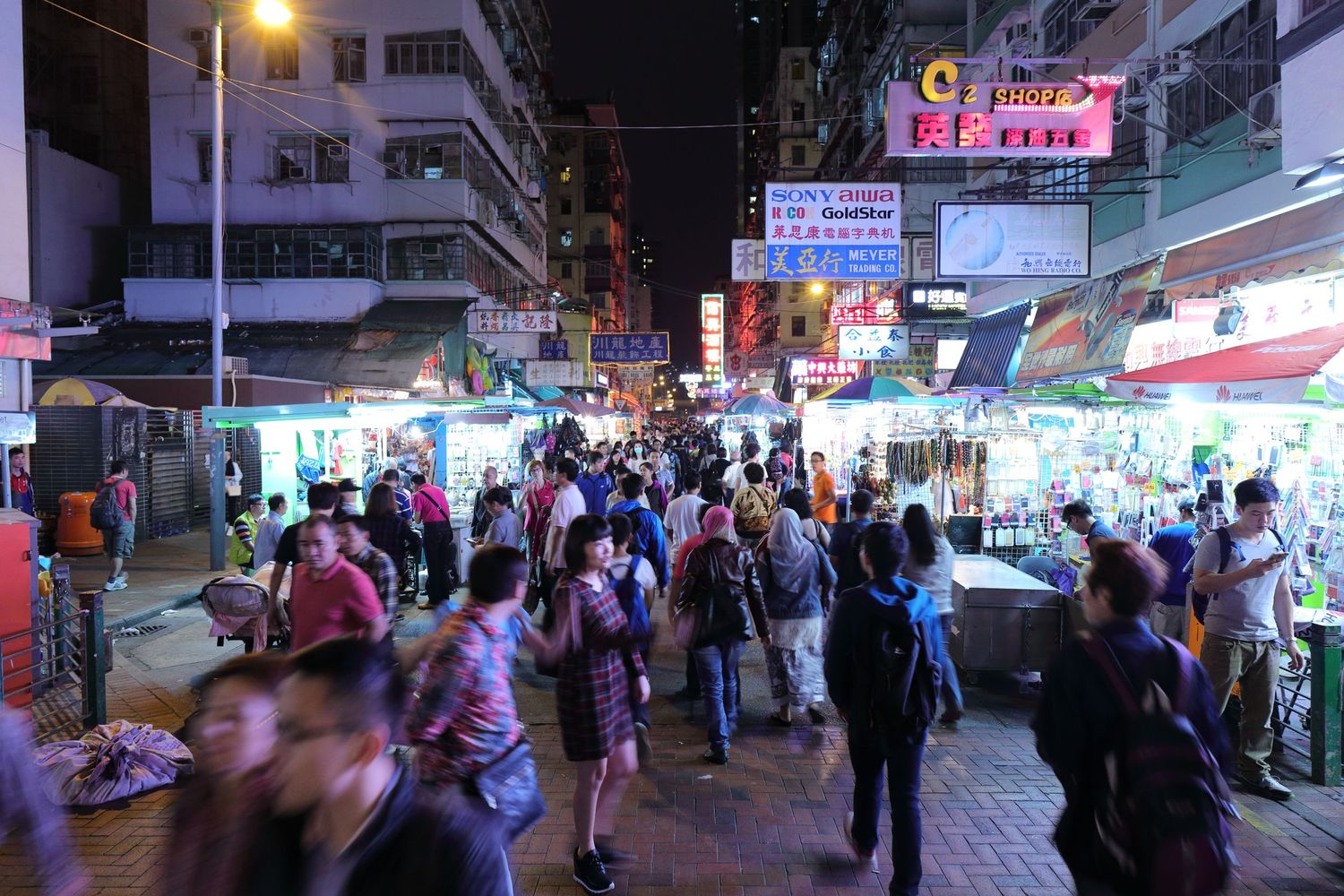 Bustling night market street scene in Hong Kong with neon signs and crowds of shoppers.