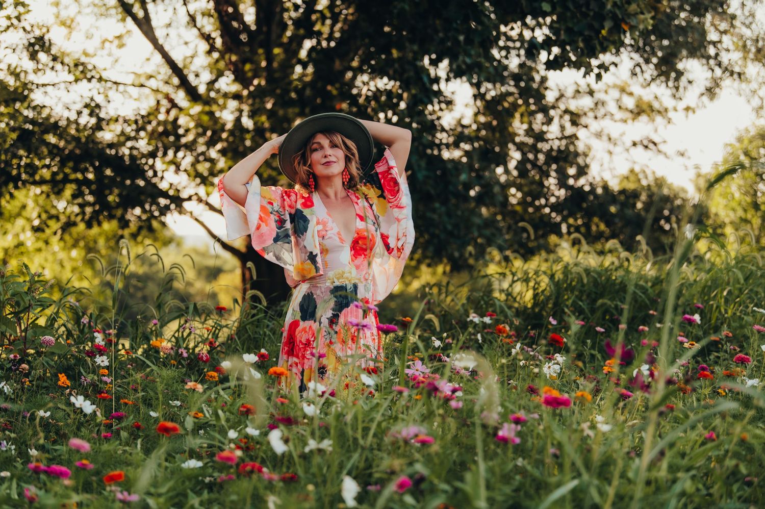 Person in floral dress stands among vibrant wildflowers during golden hour.