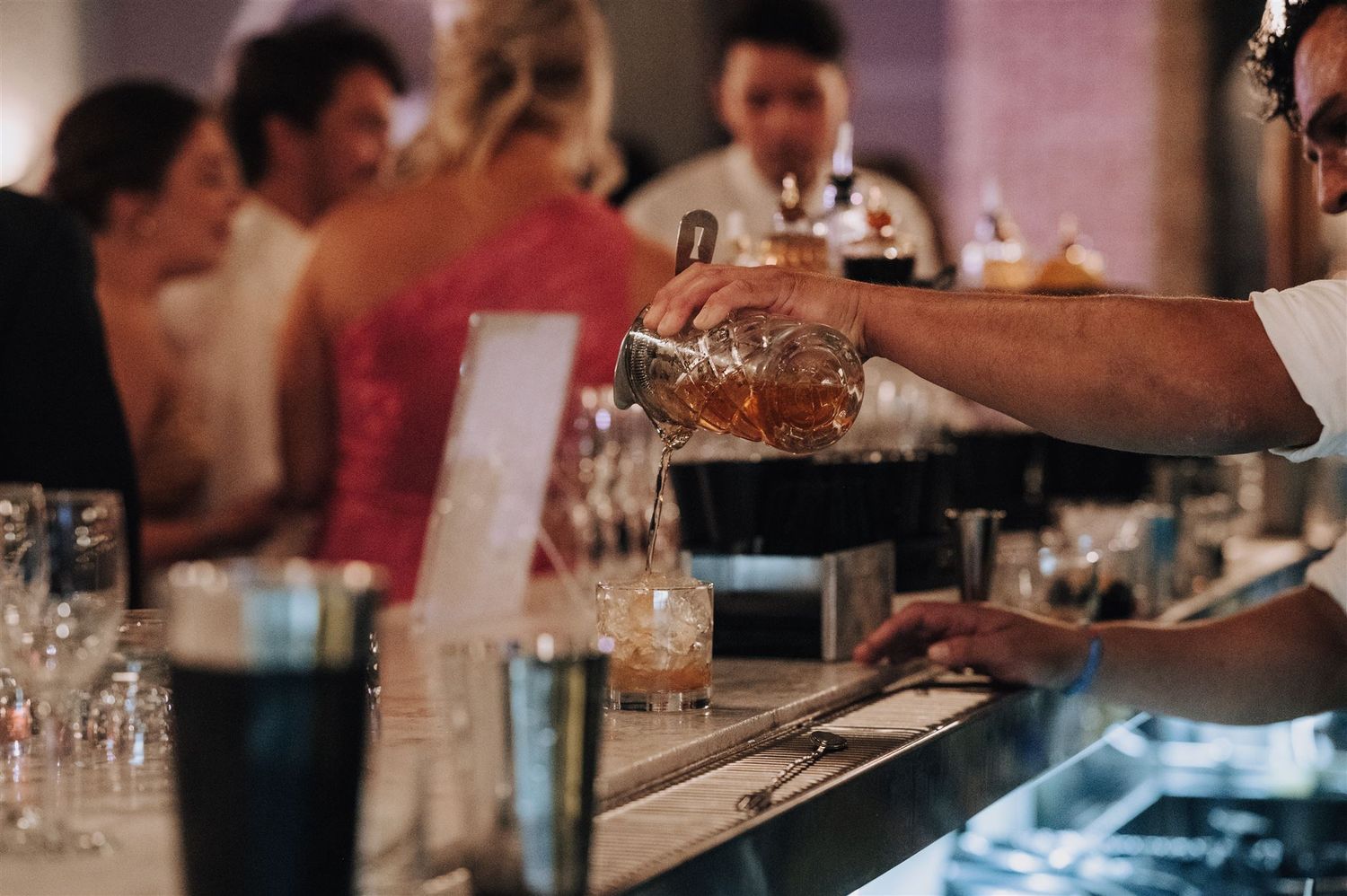 Bartender pouring drinks at an elegant wedding reception bar with glassware.