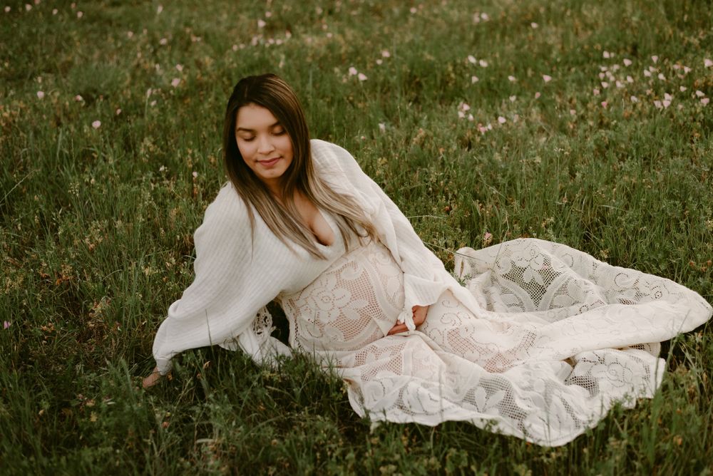 Woman in white lace dress laying in flowering meadow with dreamy atmosphere.