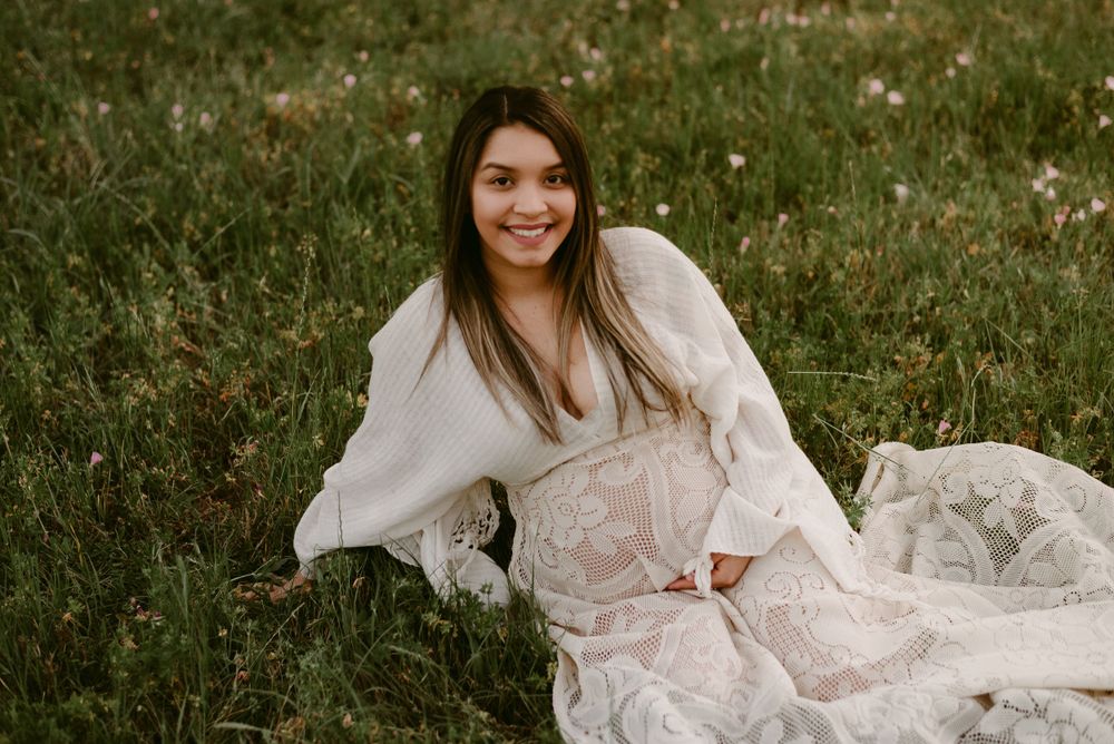 A radiant maternity portrait featuring a white lace dress in an outdoor setting.