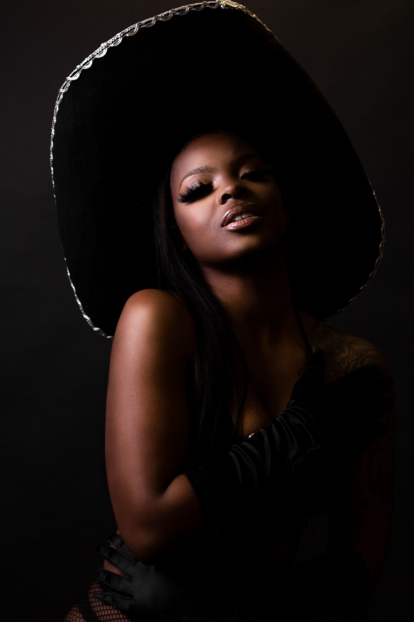 Dramatic portrait with wide brim hat against dark background.