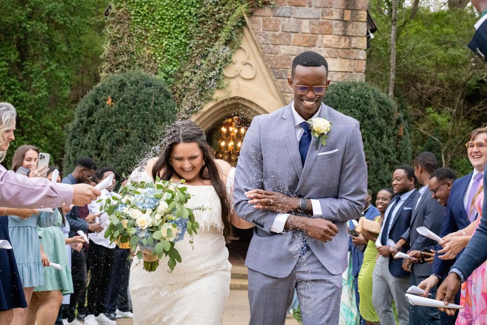 a bride and groom leave the chapel, arm in arm, as their family and friends throw congratulatory bird seed over the pair