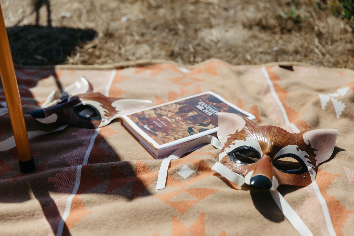 Wedding accessories and artwork scattered on an orange blanket in outdoor lighting.