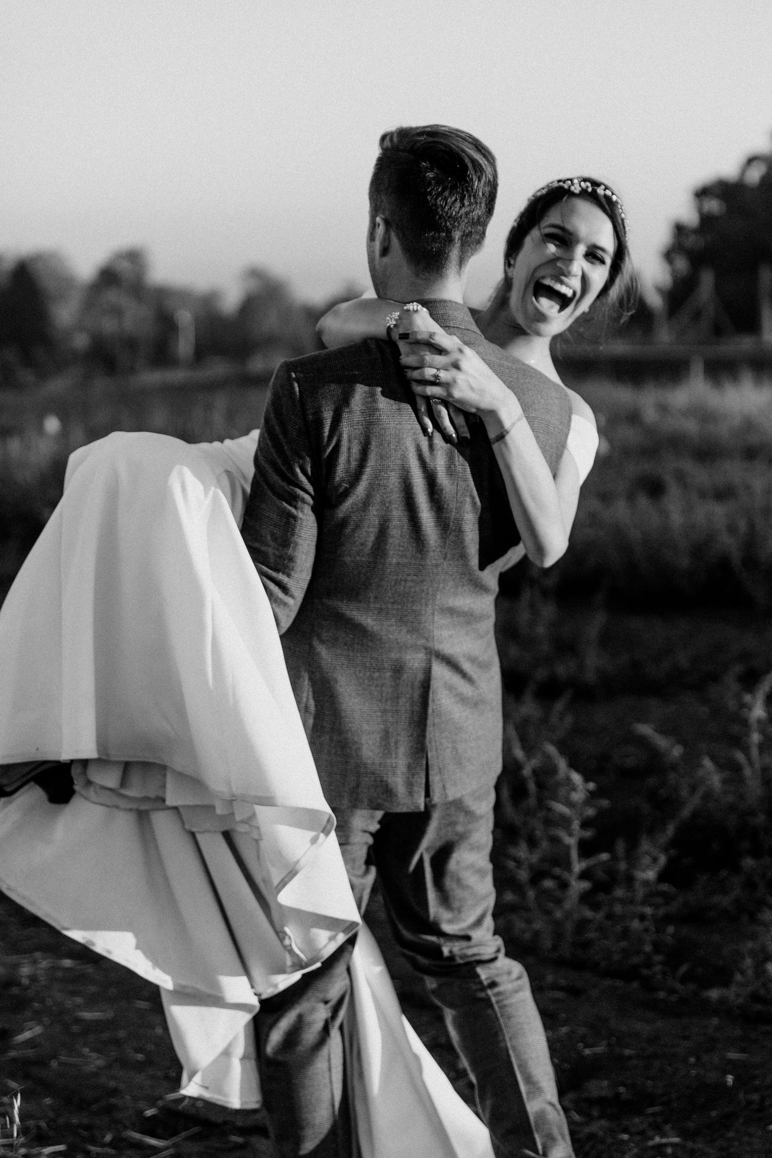 Candid black and white photo of newlyweds sharing a joyful moment outdoors.