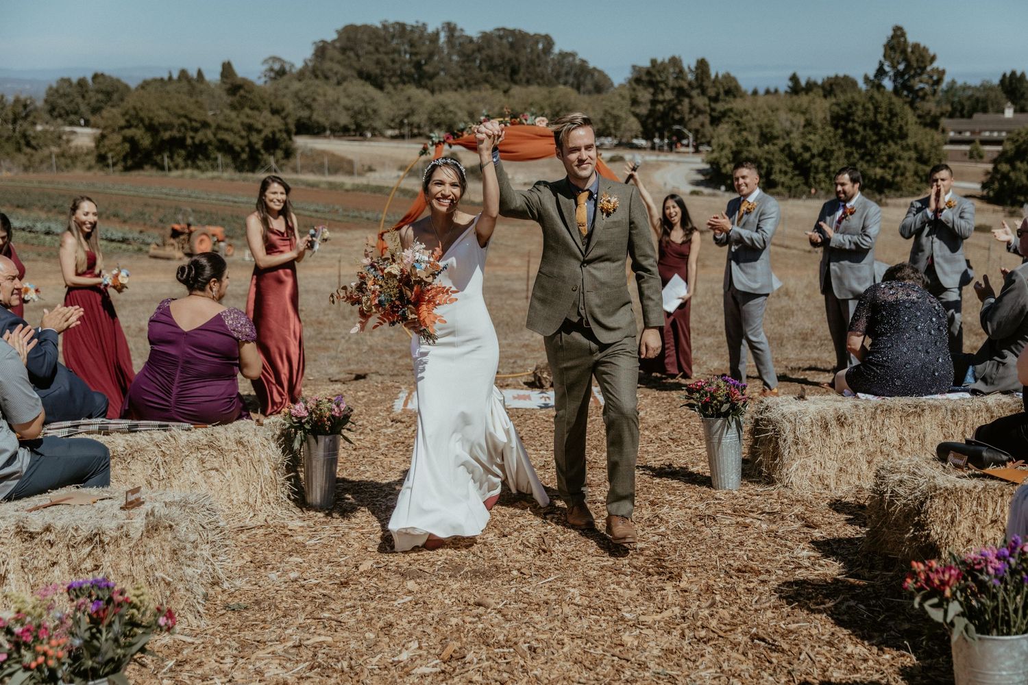 Outdoor wedding ceremony on hay bales with burgundy and floral decorations.