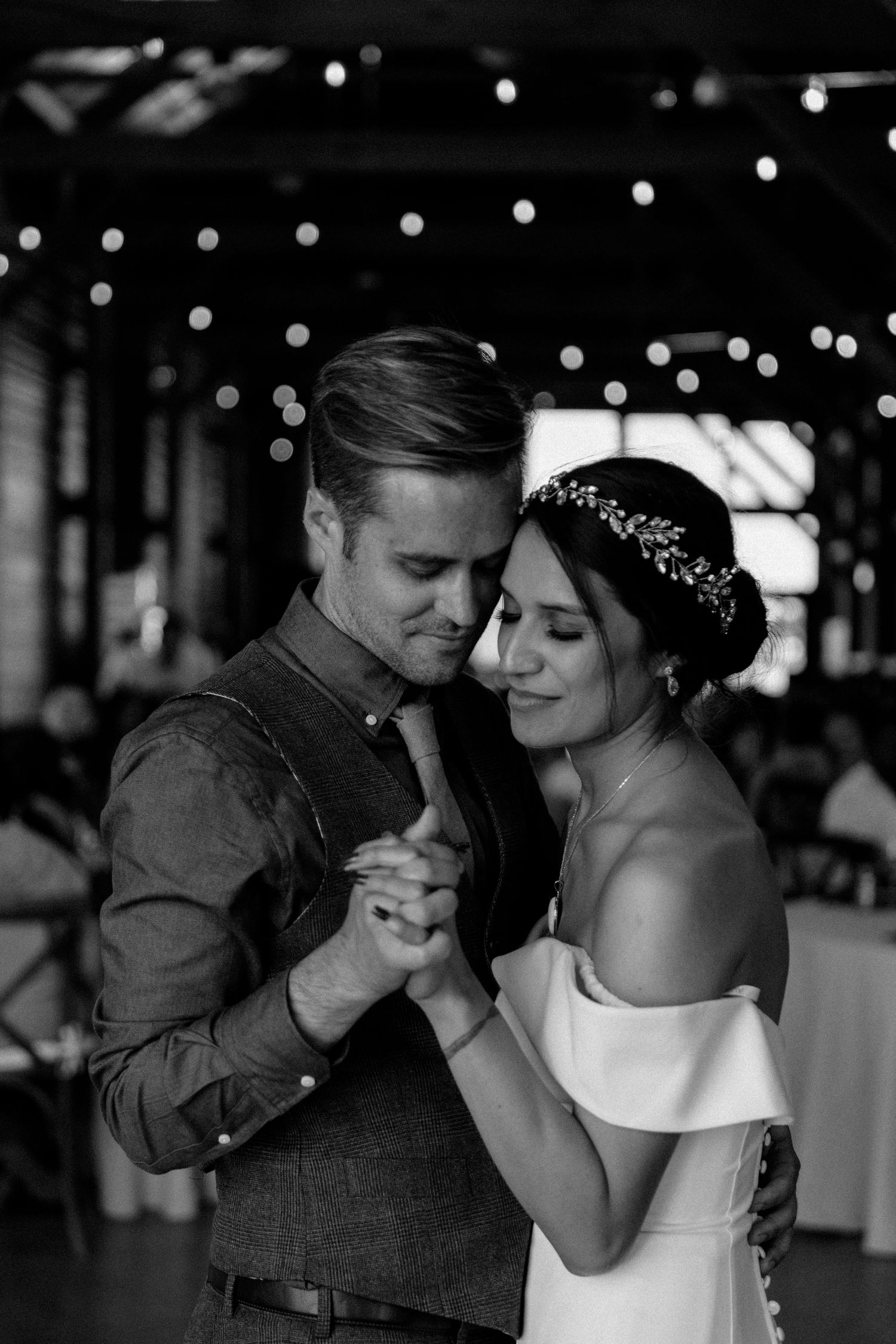 Black and white photo of couple sharing first dance under string lights.