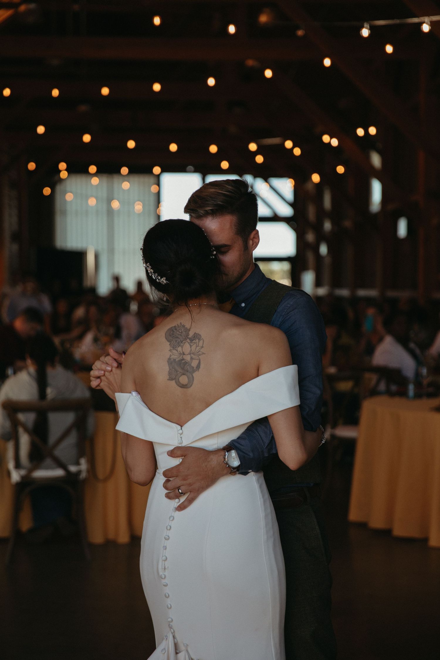 A couple dances under warm string lights in a rustic barn reception venue.