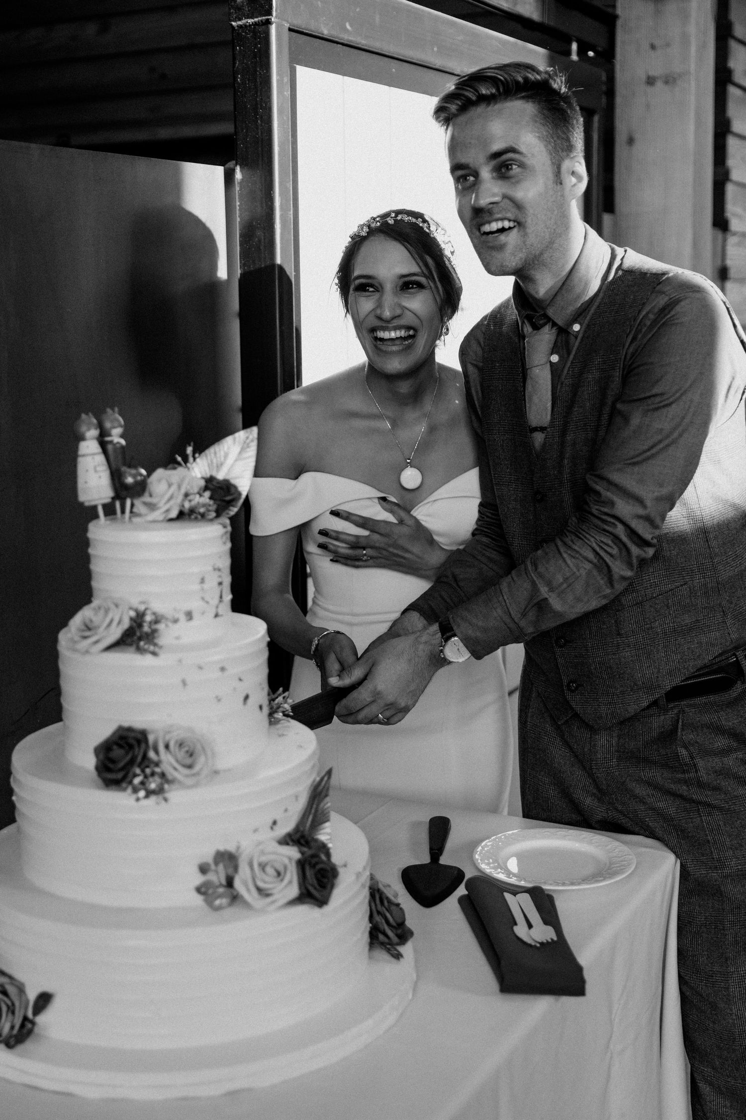 Couple cutting an elegant white tiered wedding cake decorated with roses.