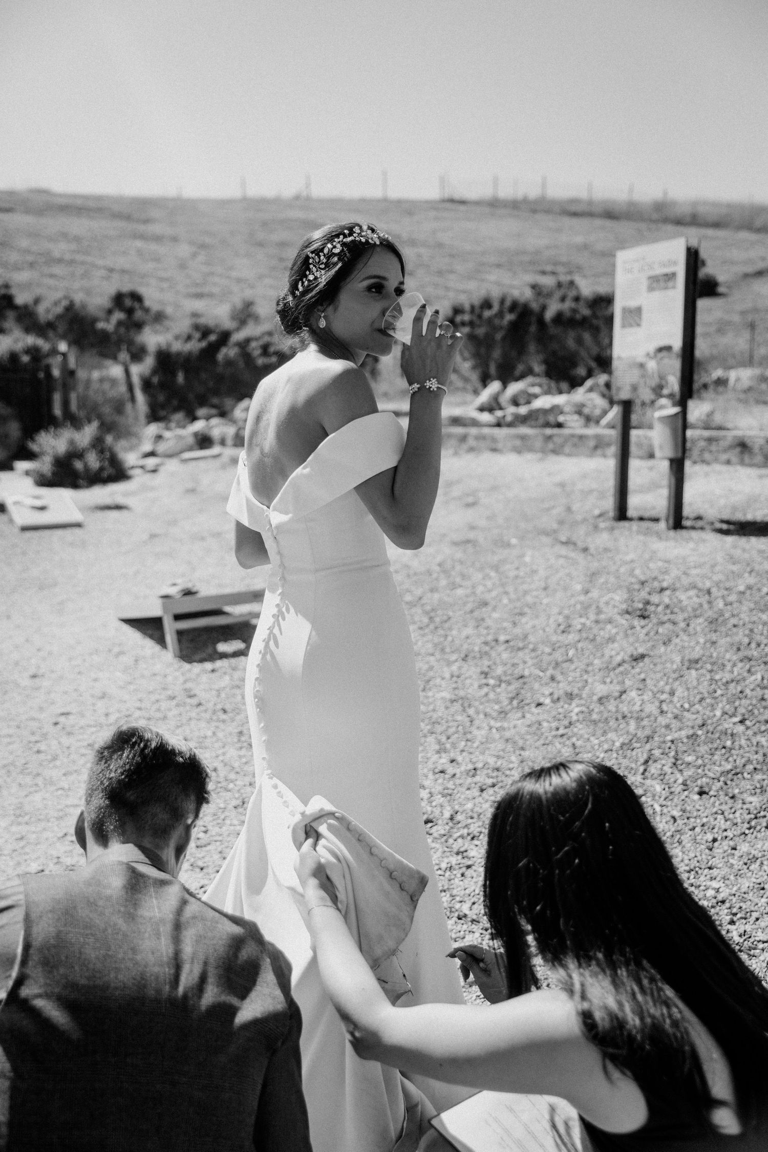 Black and white photo of final dress adjustments being made during an outdoor wedding preparation.