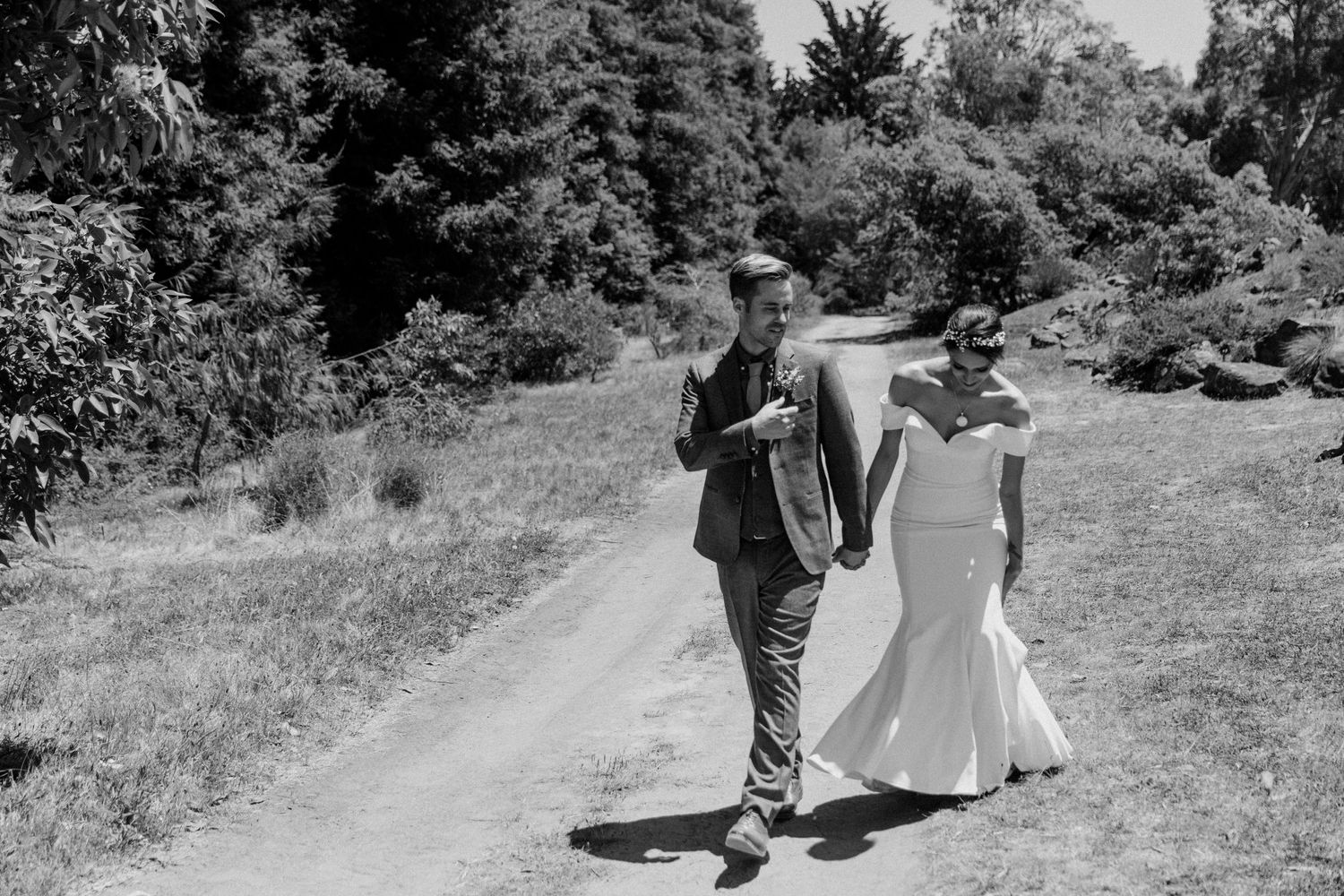 A black and white photo of a couple walking down a countryside path after their wedding ceremony.