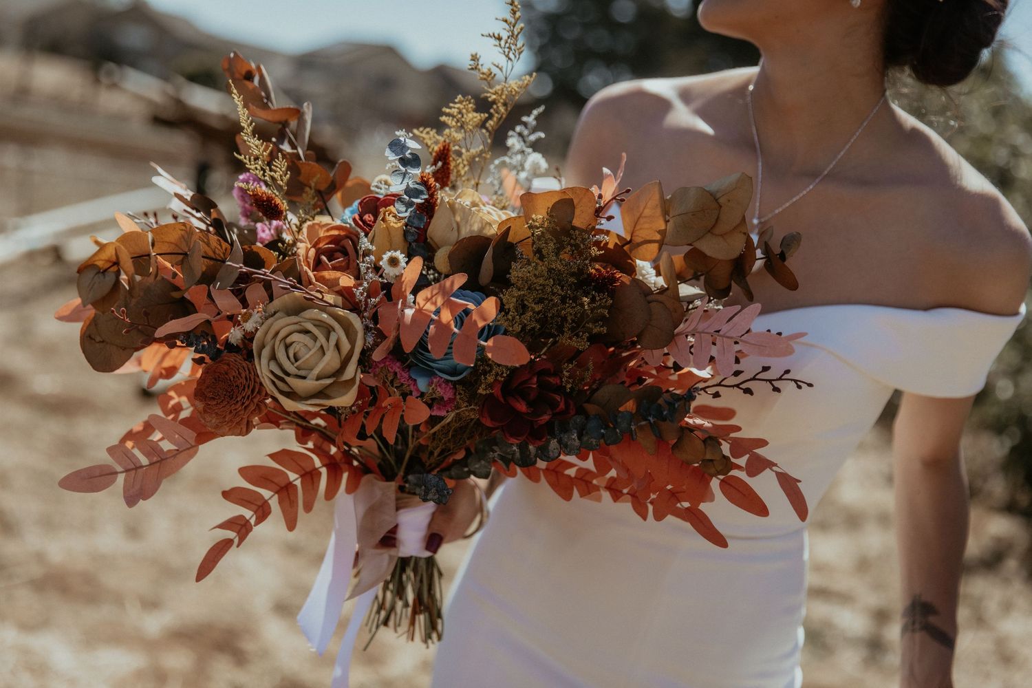 Close-up of an autumnal wedding bouquet with dried flowers and rustic elements against a white dress.