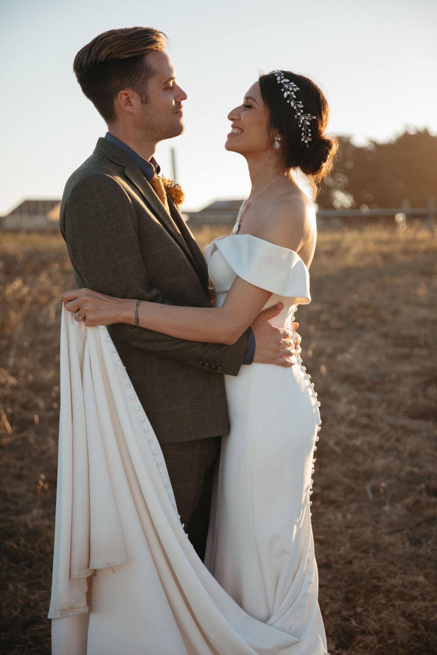 Sunset portrait of wedding couple embracing in formal attire against rural backdrop.