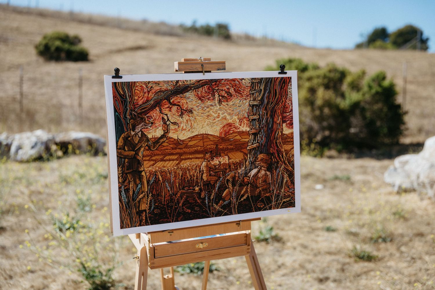 A vibrant landscape painting displayed on an easel outdoors with desert scenery in the background.