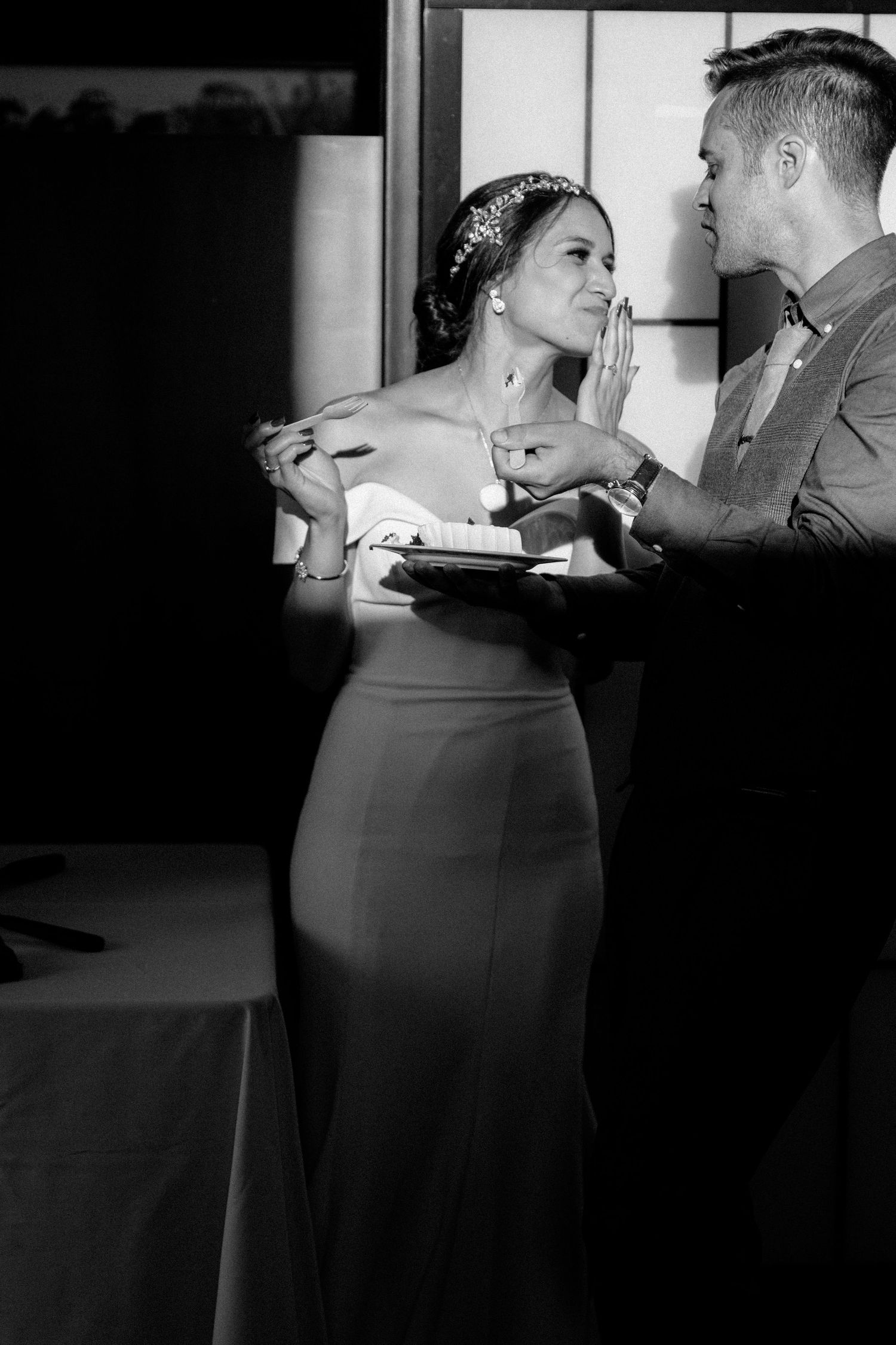 Black and white photo of couple sharing dessert during wedding reception.