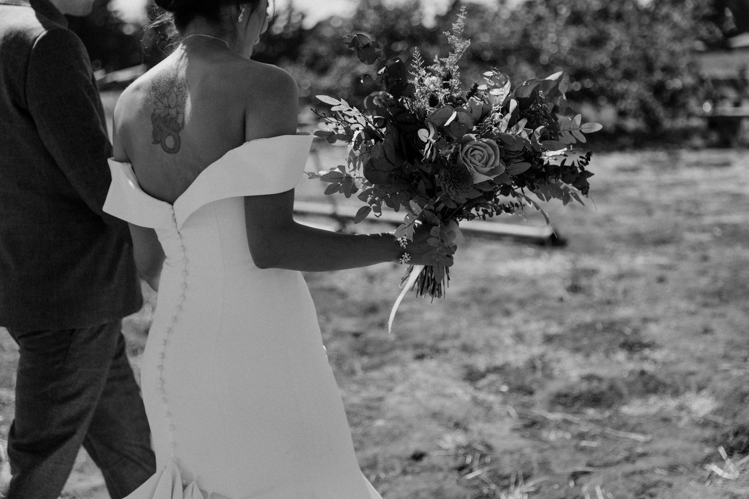 A black and white photo showing a bouquet of flowers being held against a white wedding dress.