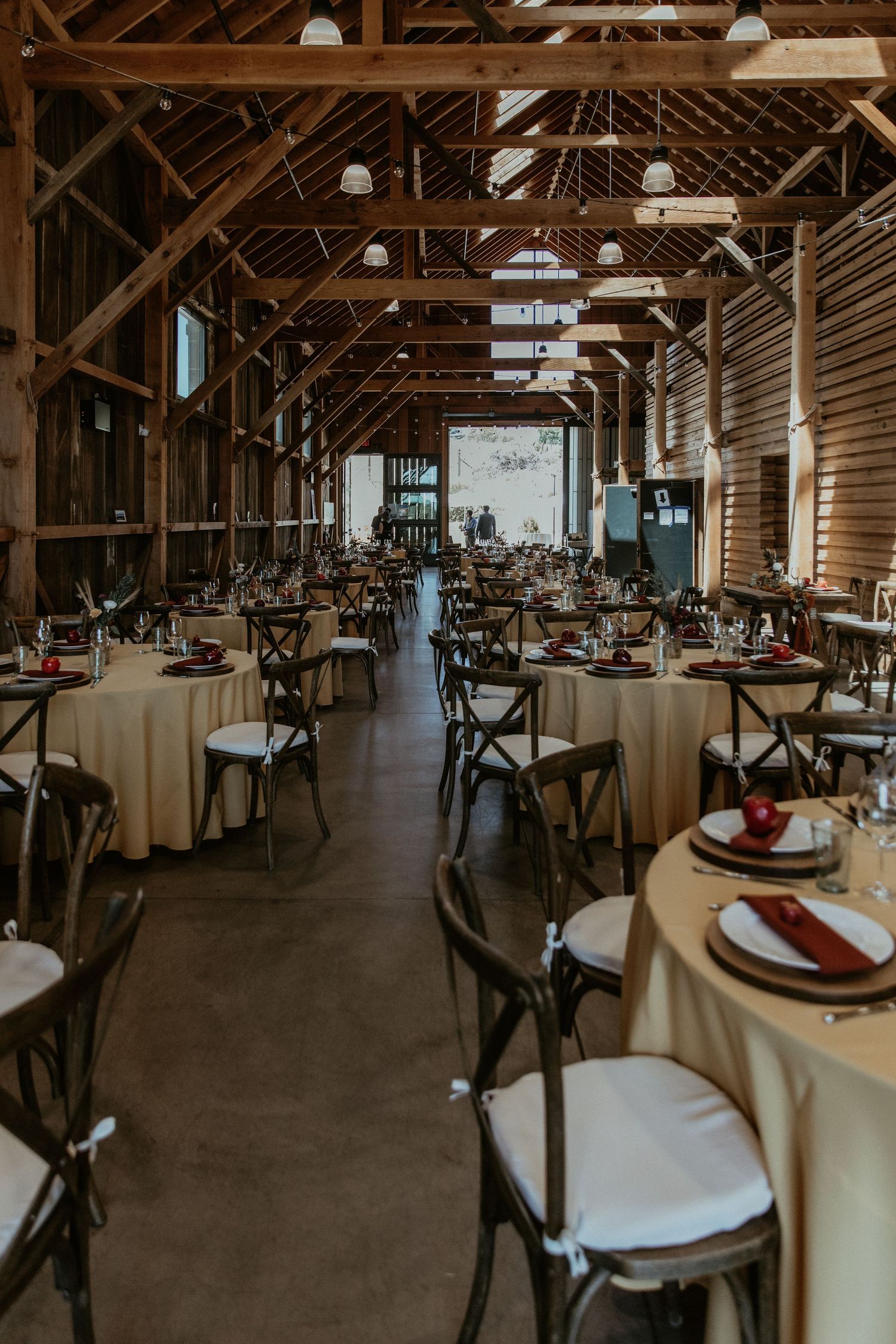 An elegant barn reception venue with wooden beams and round tables set for a wedding celebration.