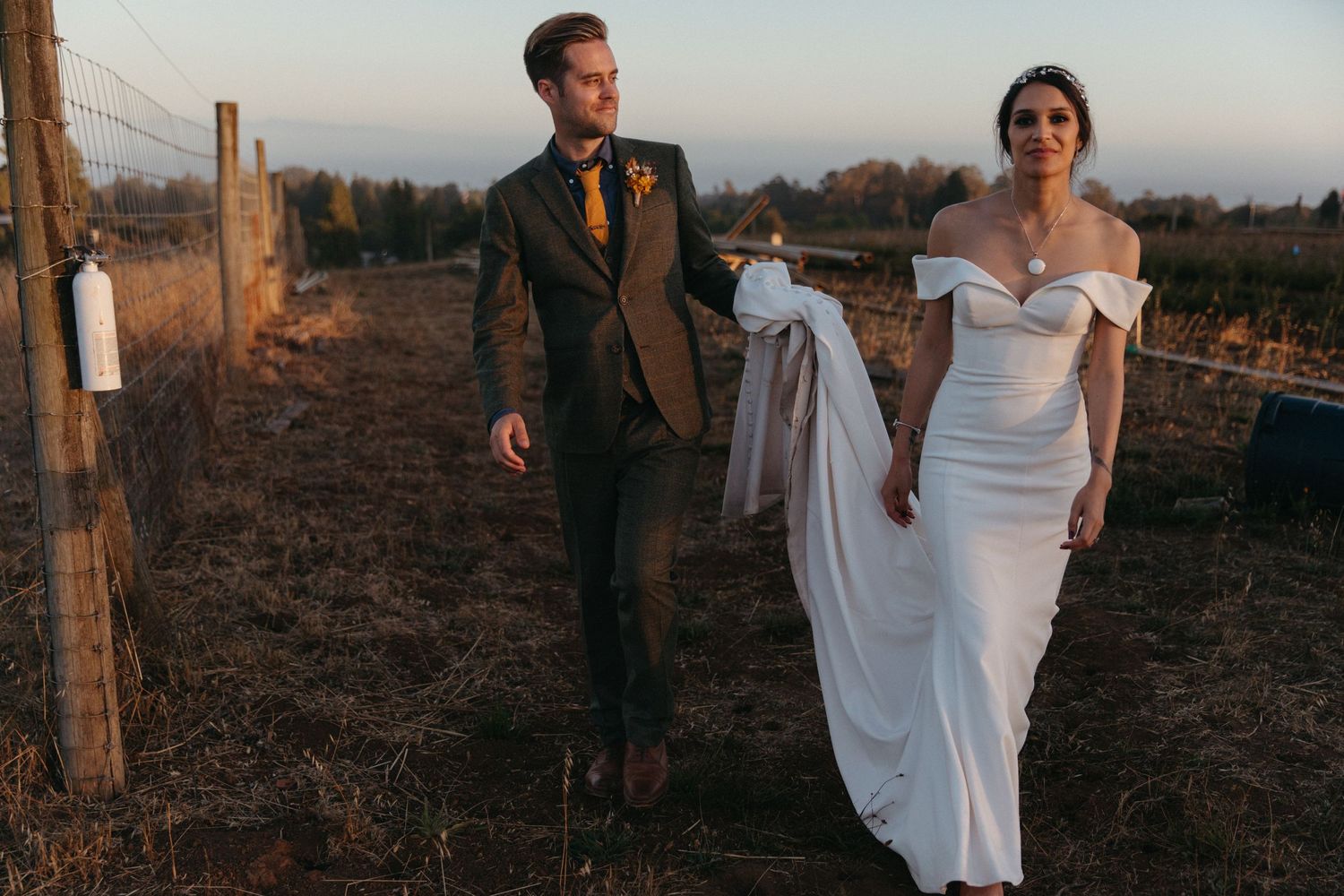 Elegant wedding couple walking through a rustic vineyard at golden hour.