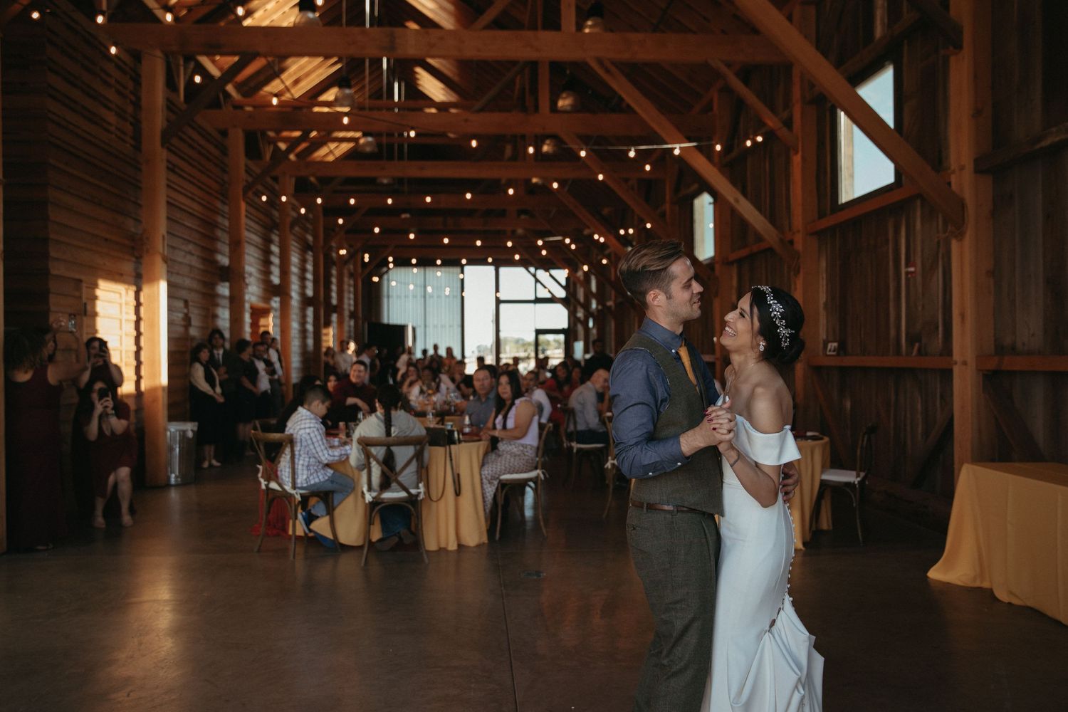 Wedding reception inside rustic barn with string lights and couples first dance.