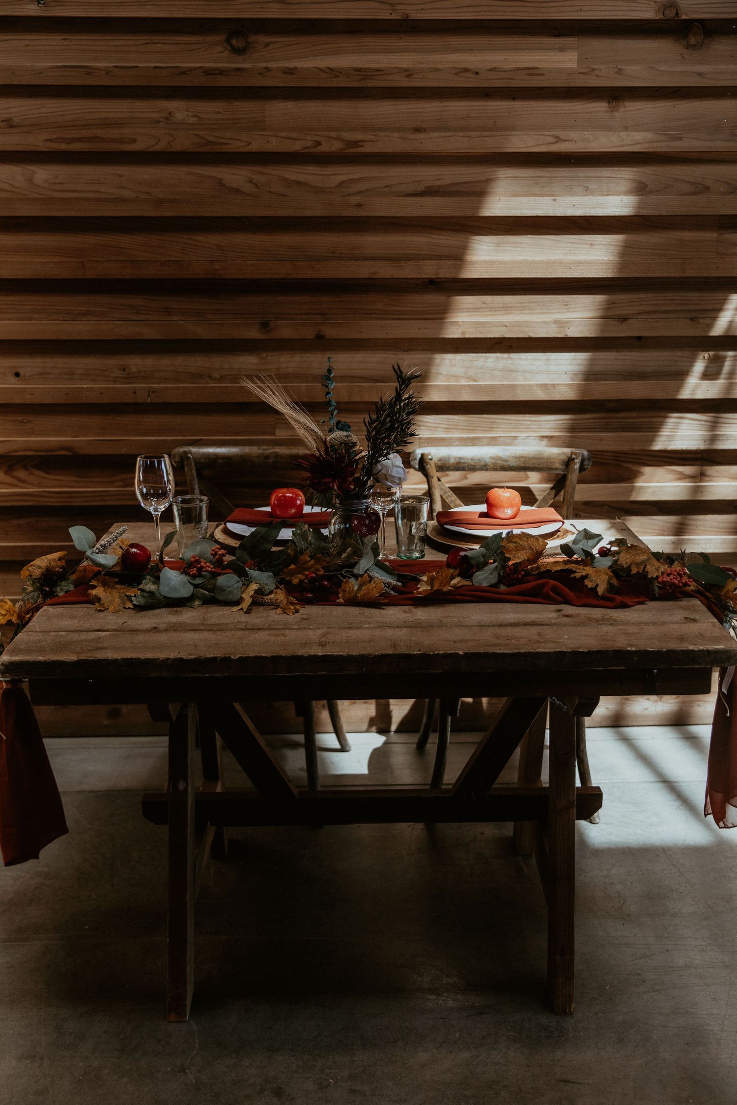 A rustic wedding table setting with vintage decor, wine glasses, and fruit in dramatic lighting.