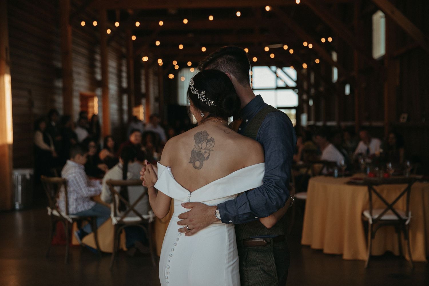 A couple embraces during their first dance in a barn reception with string lights.