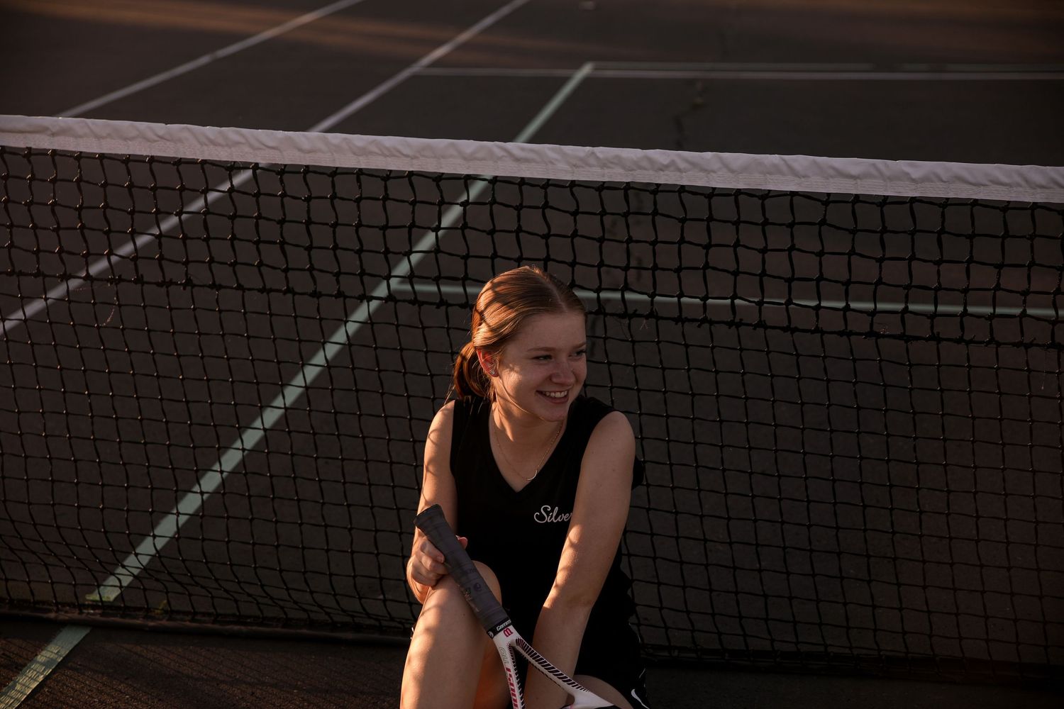 Tennis player on court at golden hour near the net in athletic wear.
