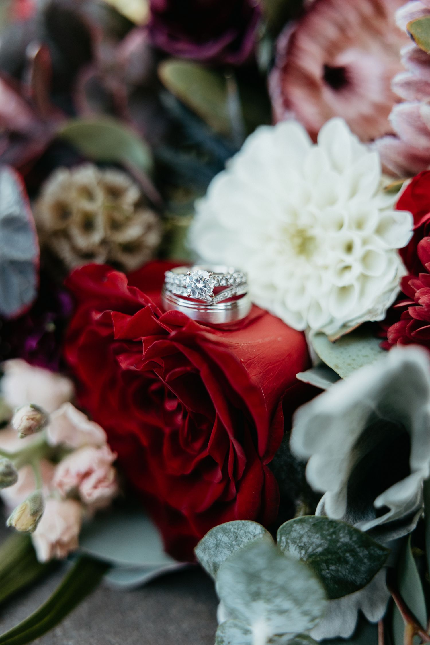 Wedding rings nestled on red and white flowers in an elegant bridal bouquet.