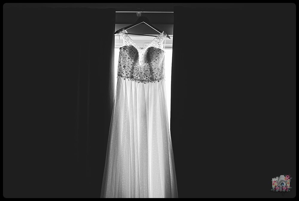 A white lace wedding dress hangs against a dark background in black and white.