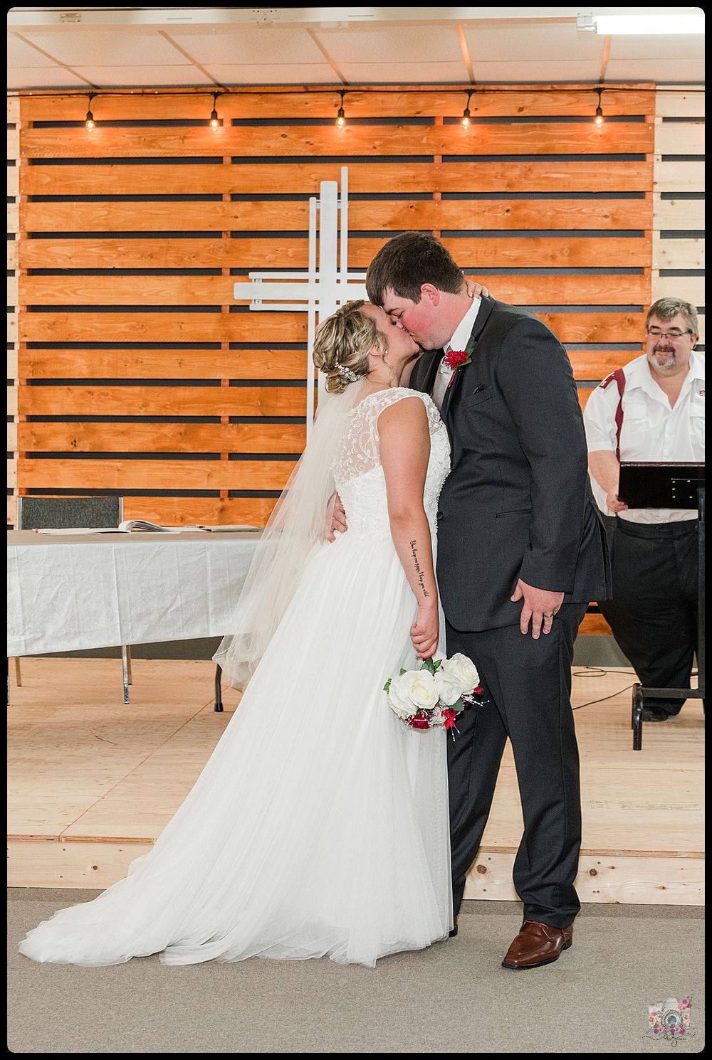 A romantic moment between newlyweds in front of a wooden wall with white cross decoration.