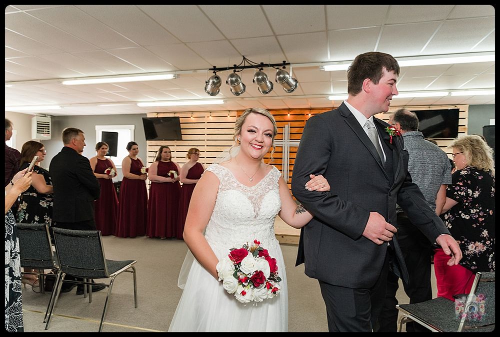 A couple walks arm in arm through a reception hall decorated with burgundy accents.